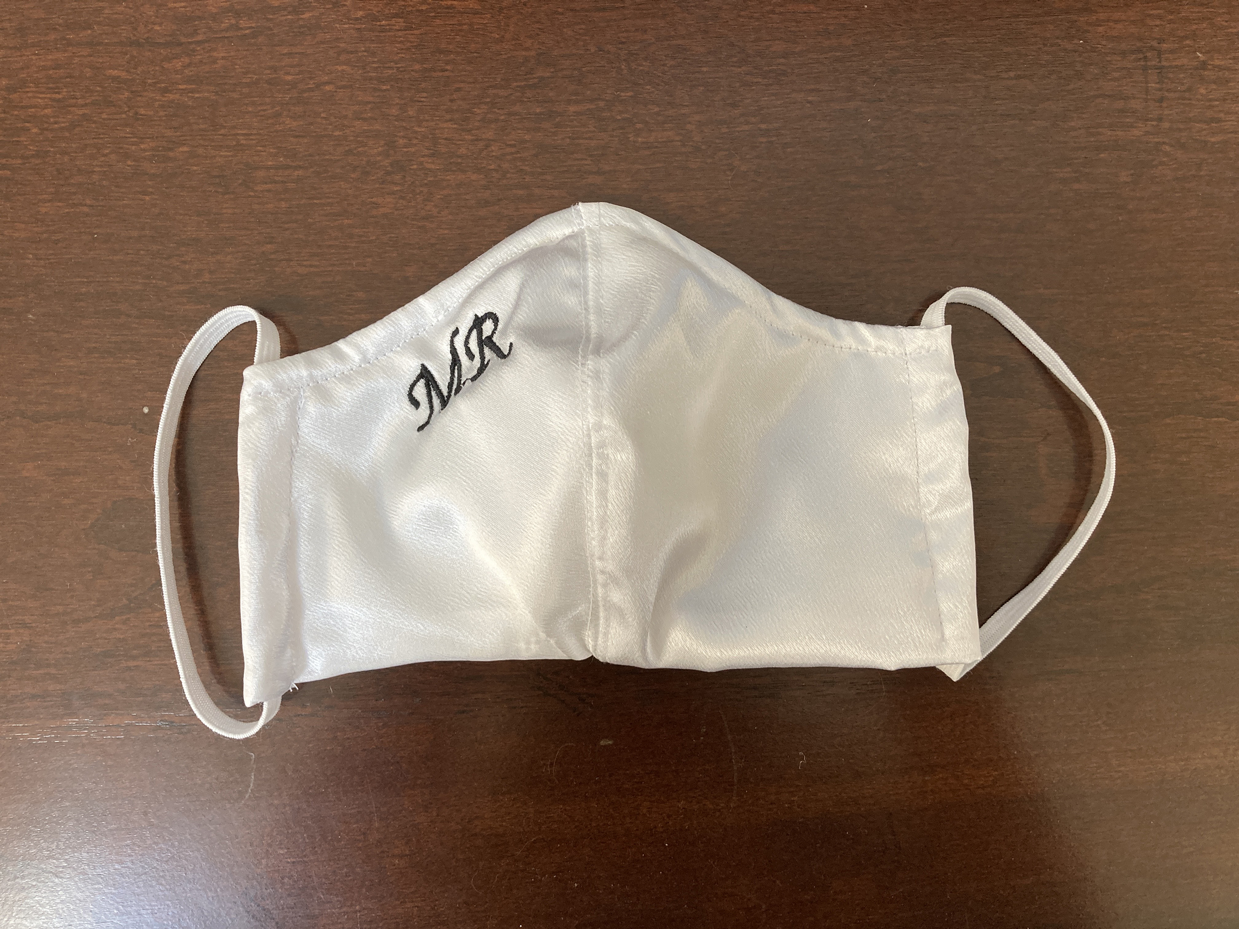 White satin mask with "MR" embroidered in black thread