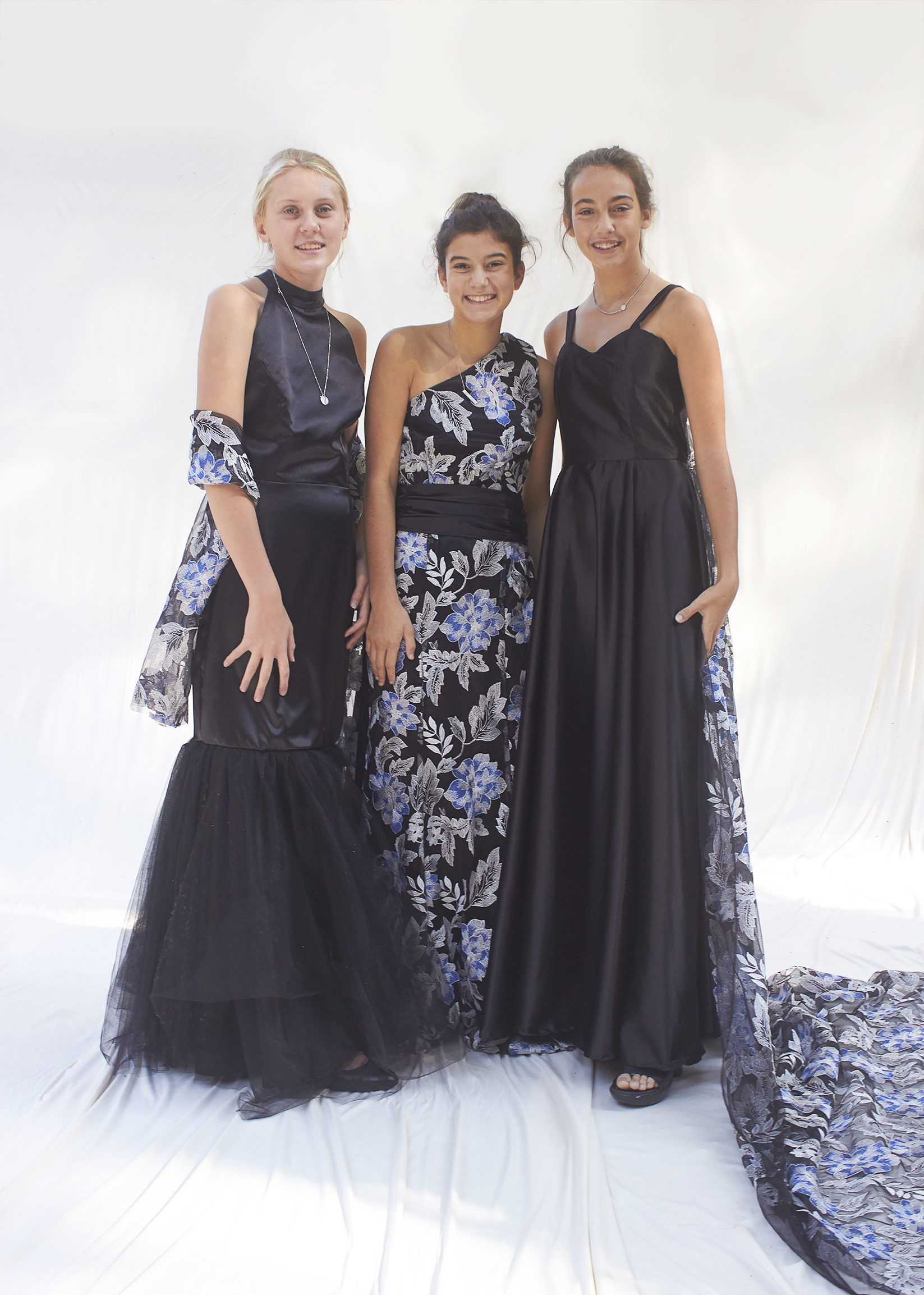 Three girls stand in black, blue, and silver evening wear gowns