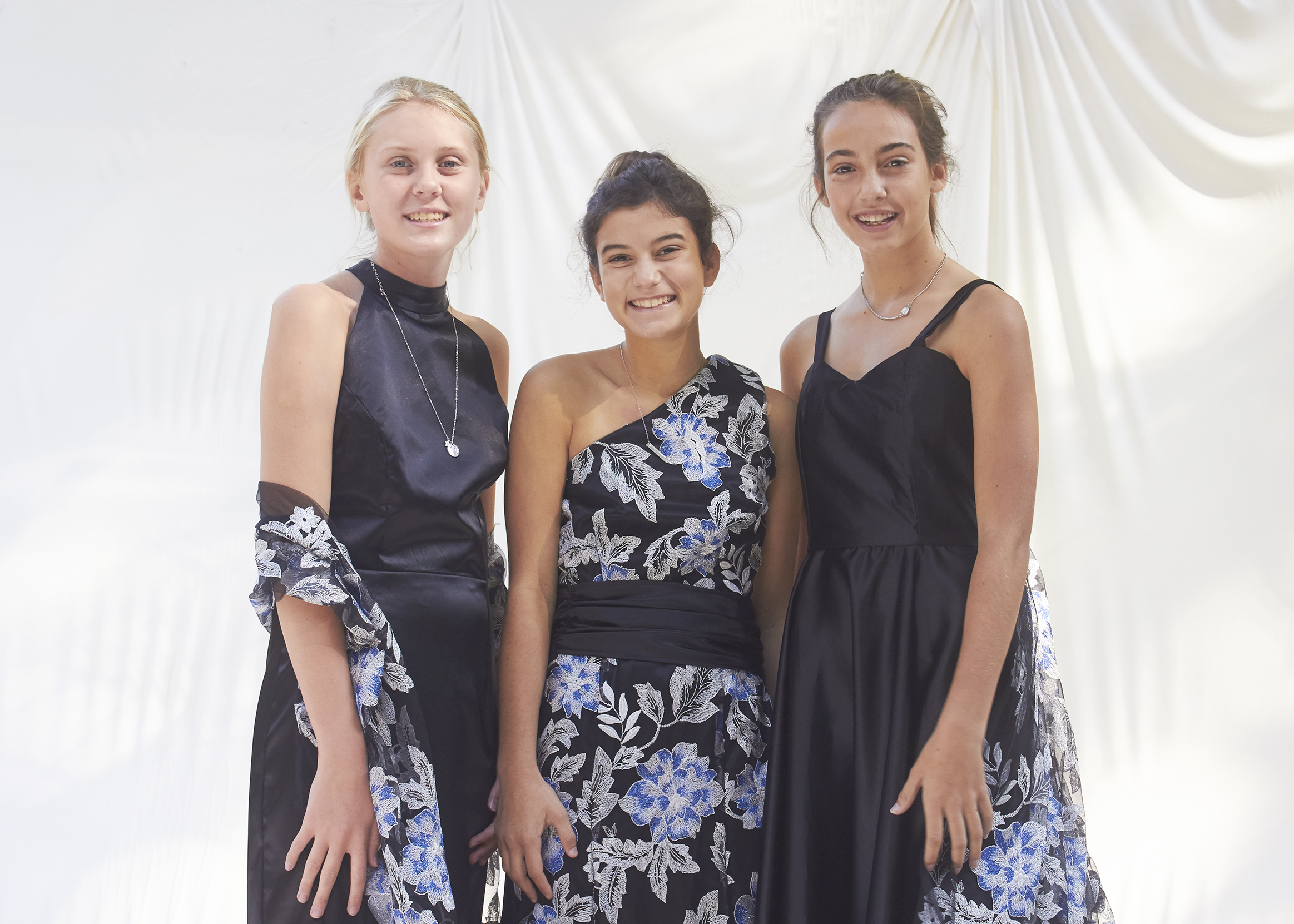 Three girls stand in similar black and silver floral brocade gowns