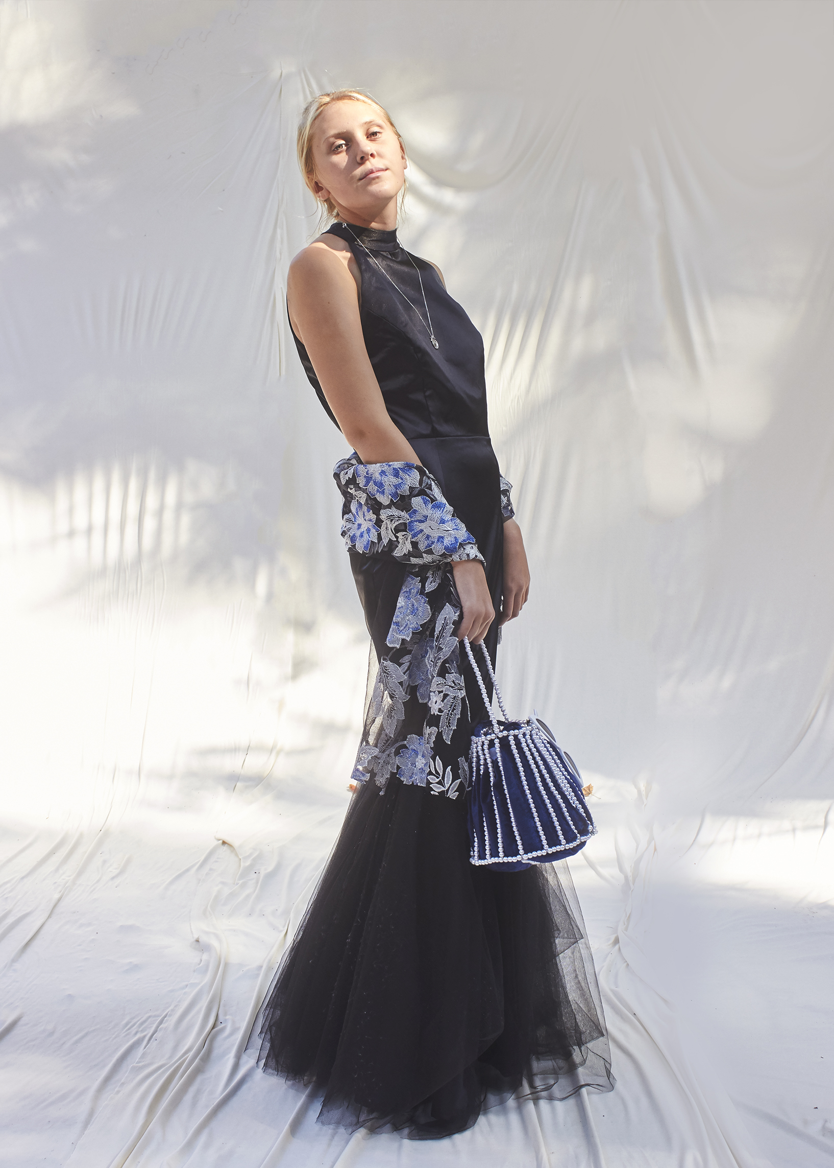 Girl stands in black trumpet gown with brocade shawl