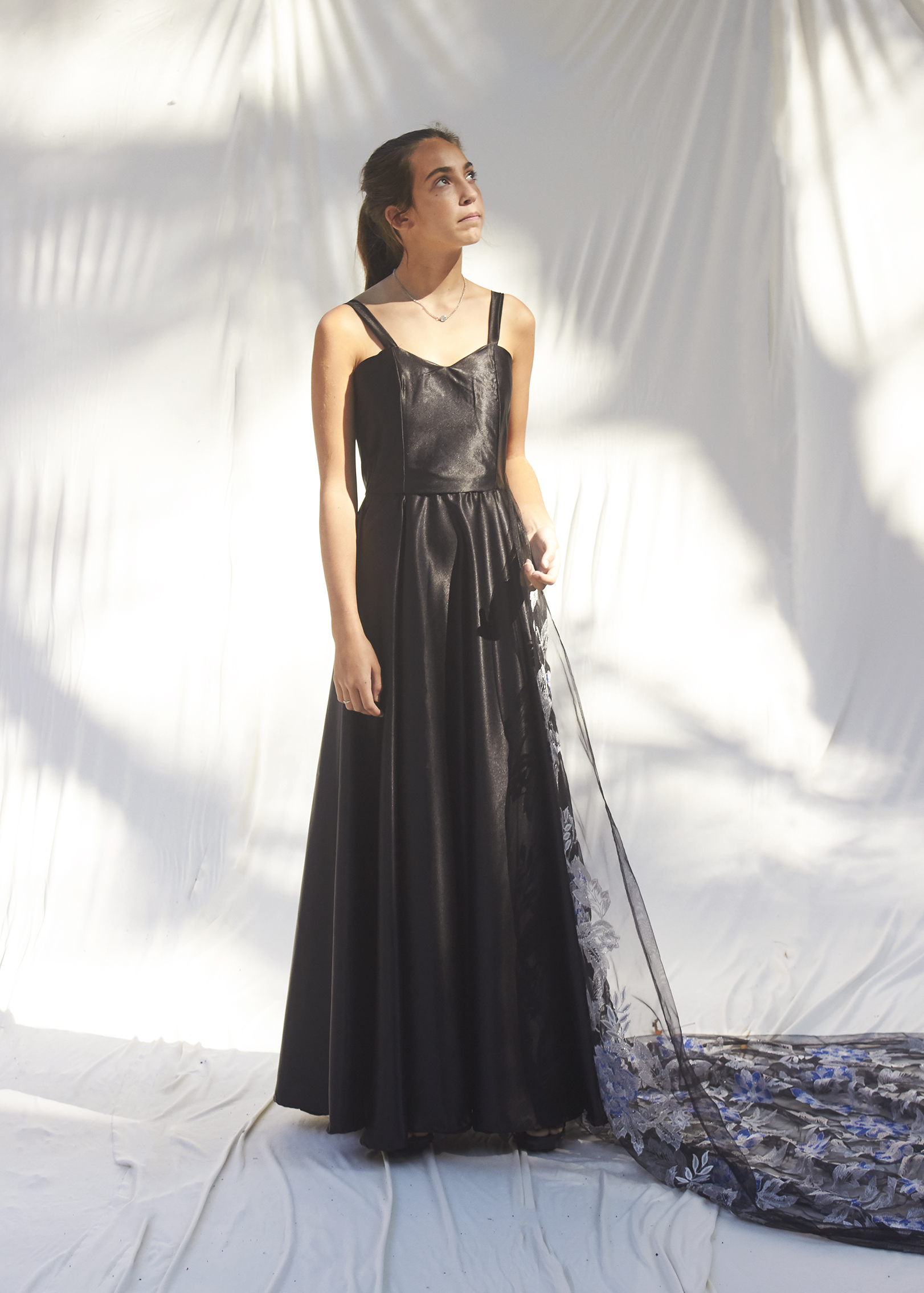 Girl stands in elegant black evening gown with a brocade silver train