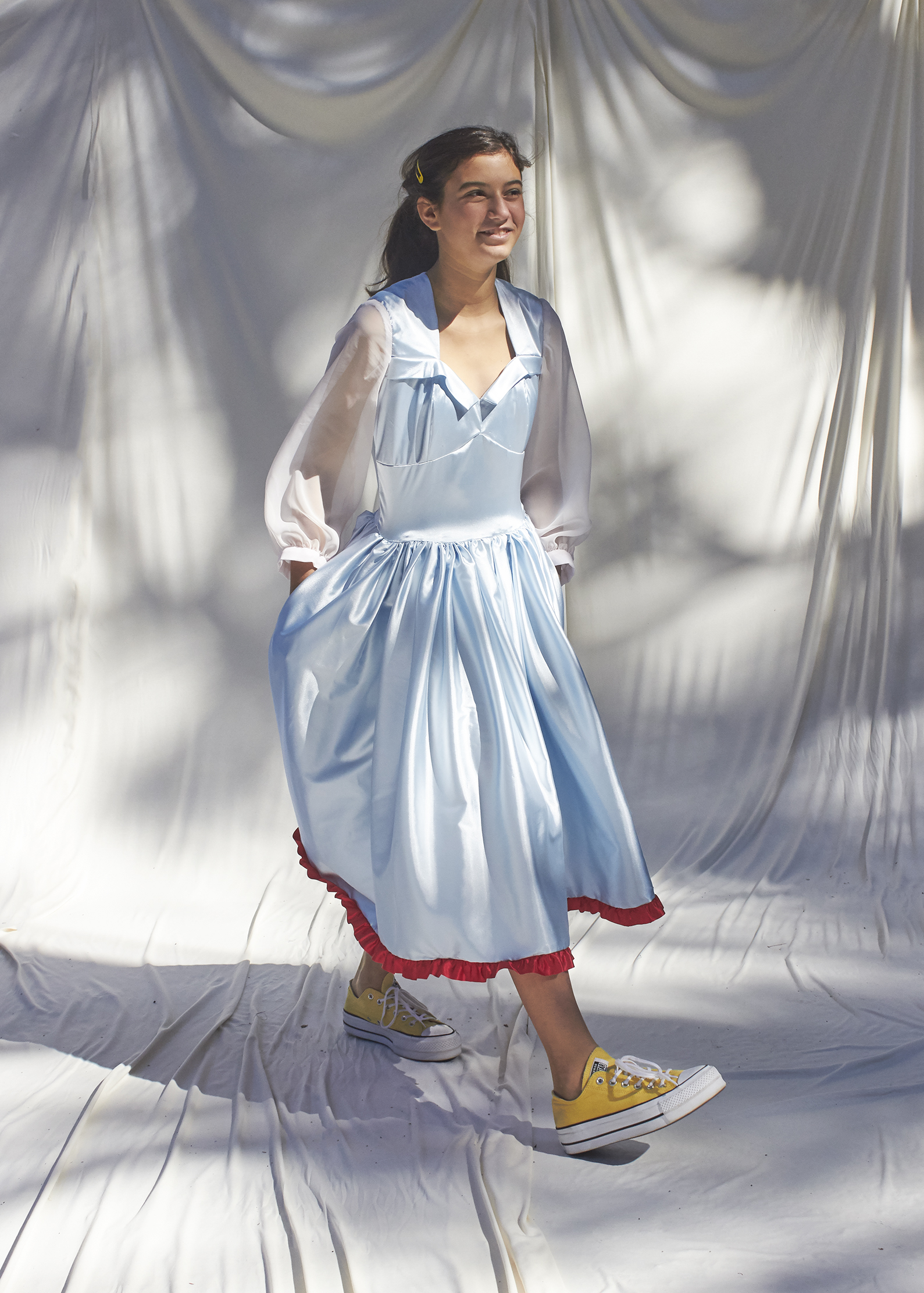 Girl walking in light blue dress with white sheer balloon sleeves and red trimmed hem