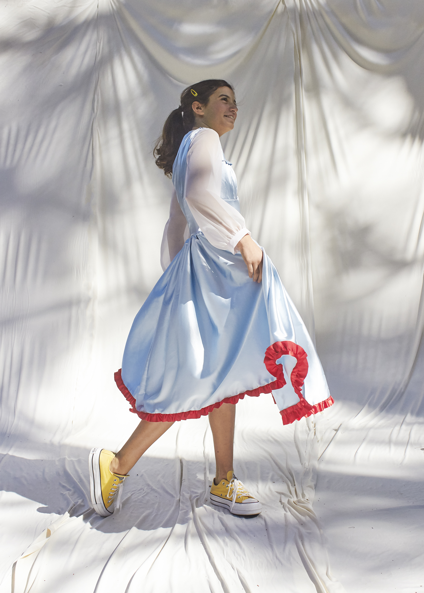 Side view of girl walking in light blue dress with white sheer balloon sleeves and red trimmed hem