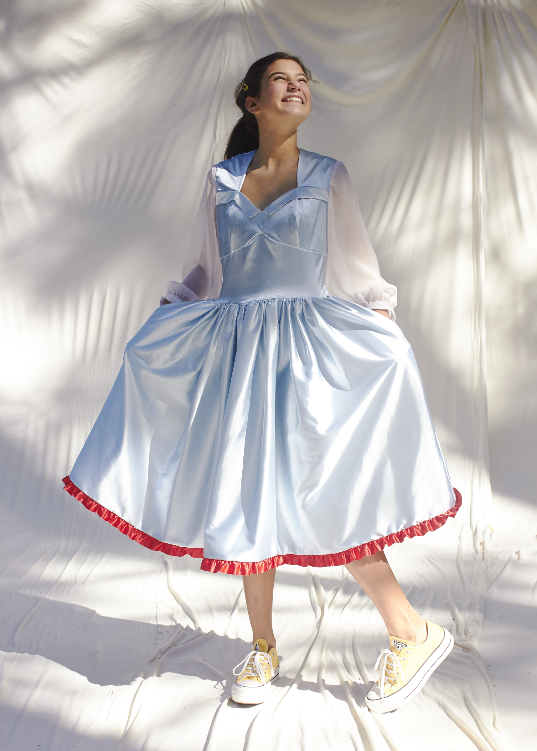 girl posing in light blue dress with white sheer balloon sleeves and red trimmed hem