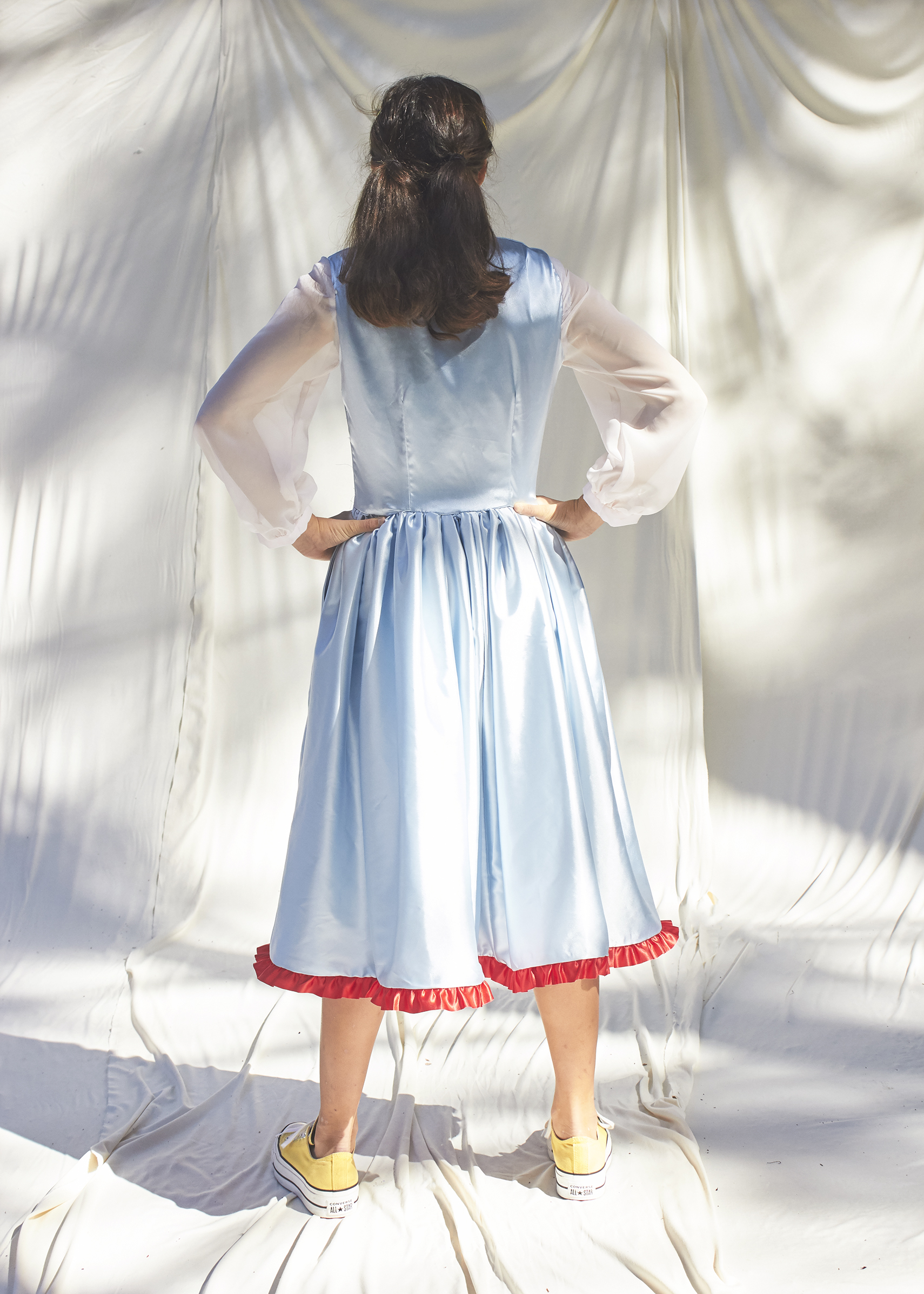 Back view girl posing in light blue dress with white sheer balloon sleeves and red trimmed hem