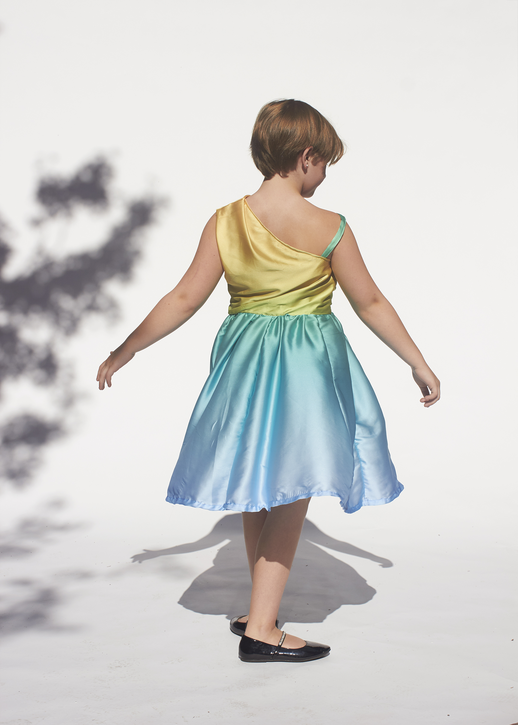 Back view of girl spinning in a one shoulder yellow and blue satin dress