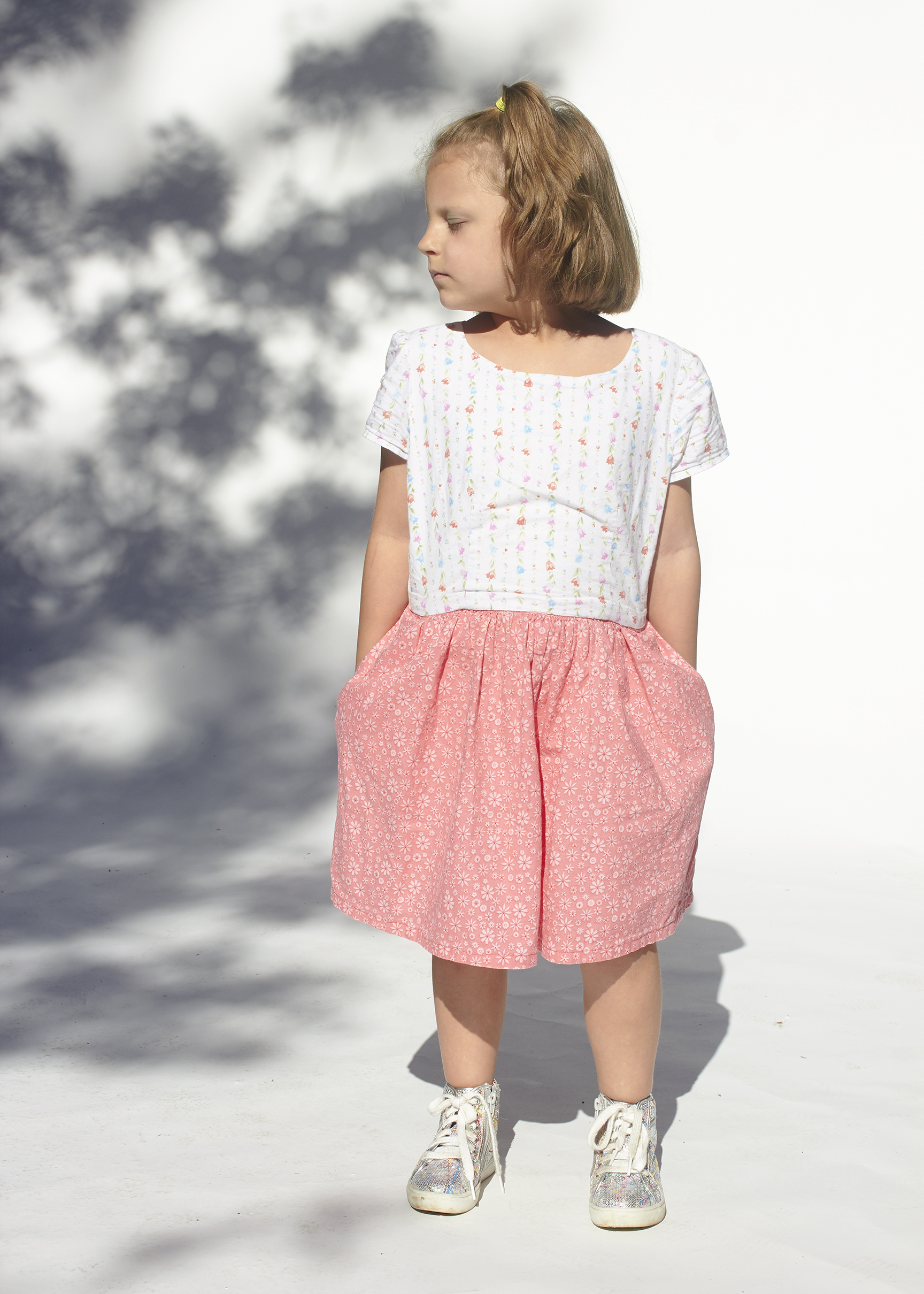 Young girl in white and pink floral dress with hand in pockets