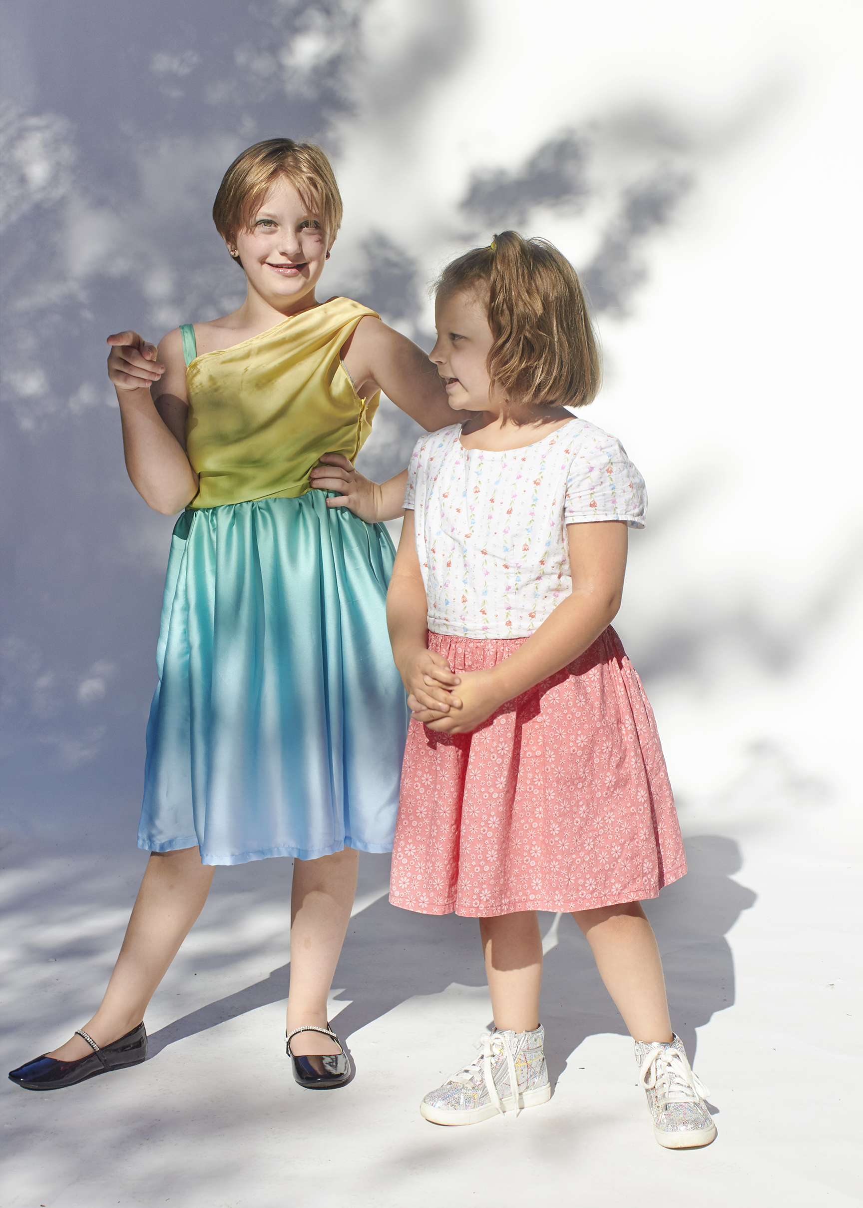 Photo to two girls, one is dressed in a sunset dress, and the other is in a floral dress.