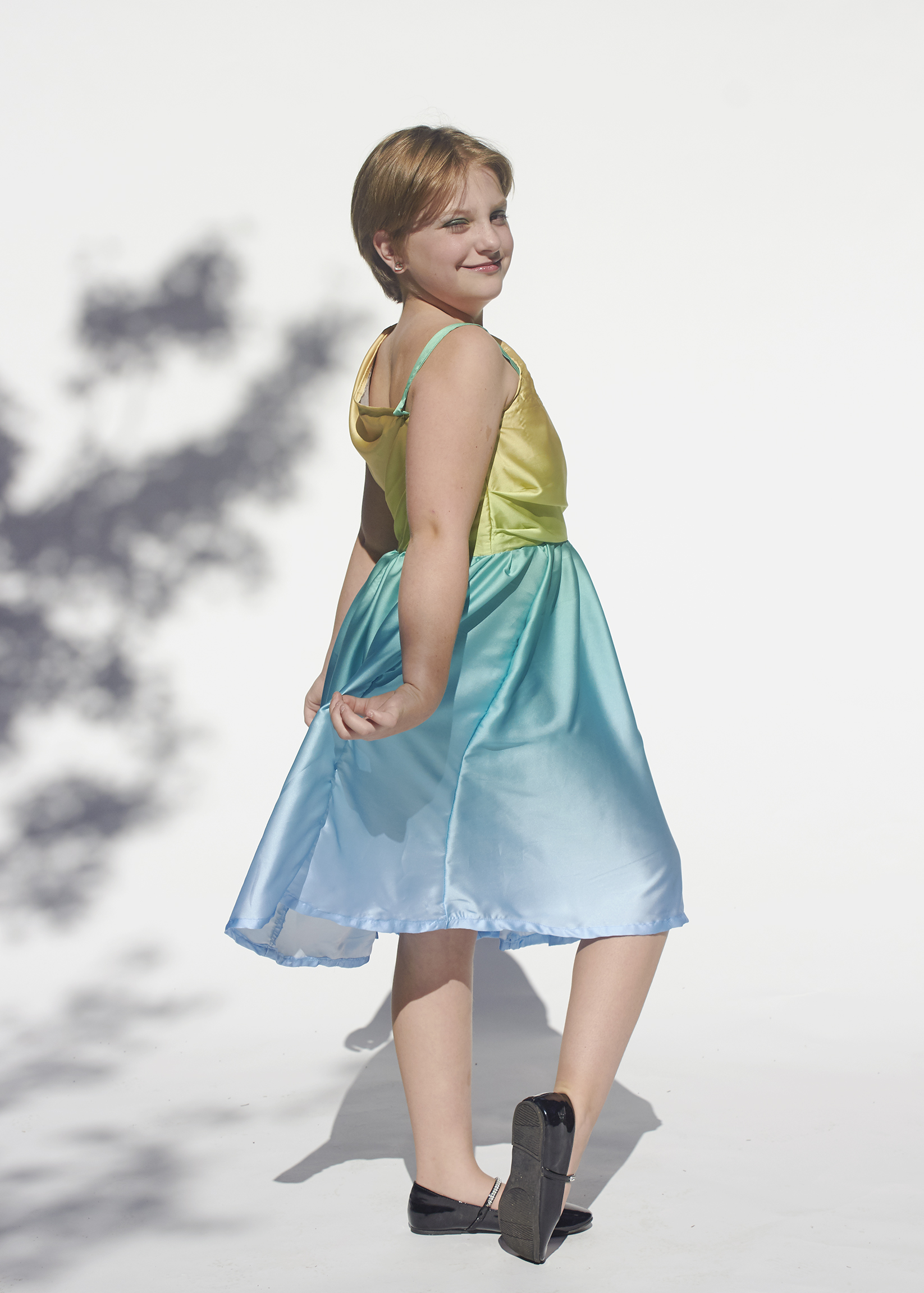 Young girl in a yellow and aqua one shoulder dress. This is a side view