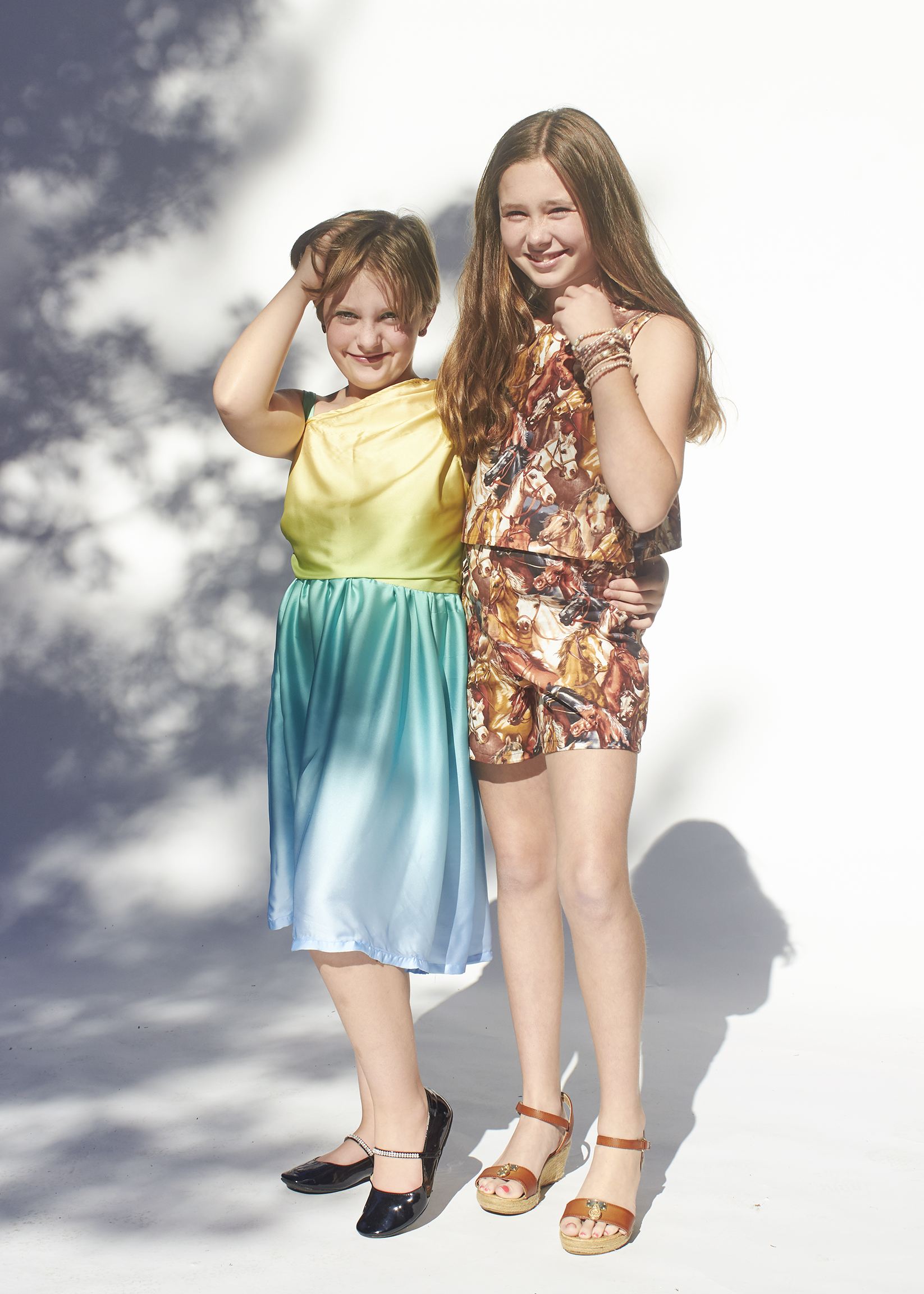 Two girls in their handmade outfits. One is in a one shoulder ombre blue and yellow dress, and the other rigor is dress in a horse printed matching set