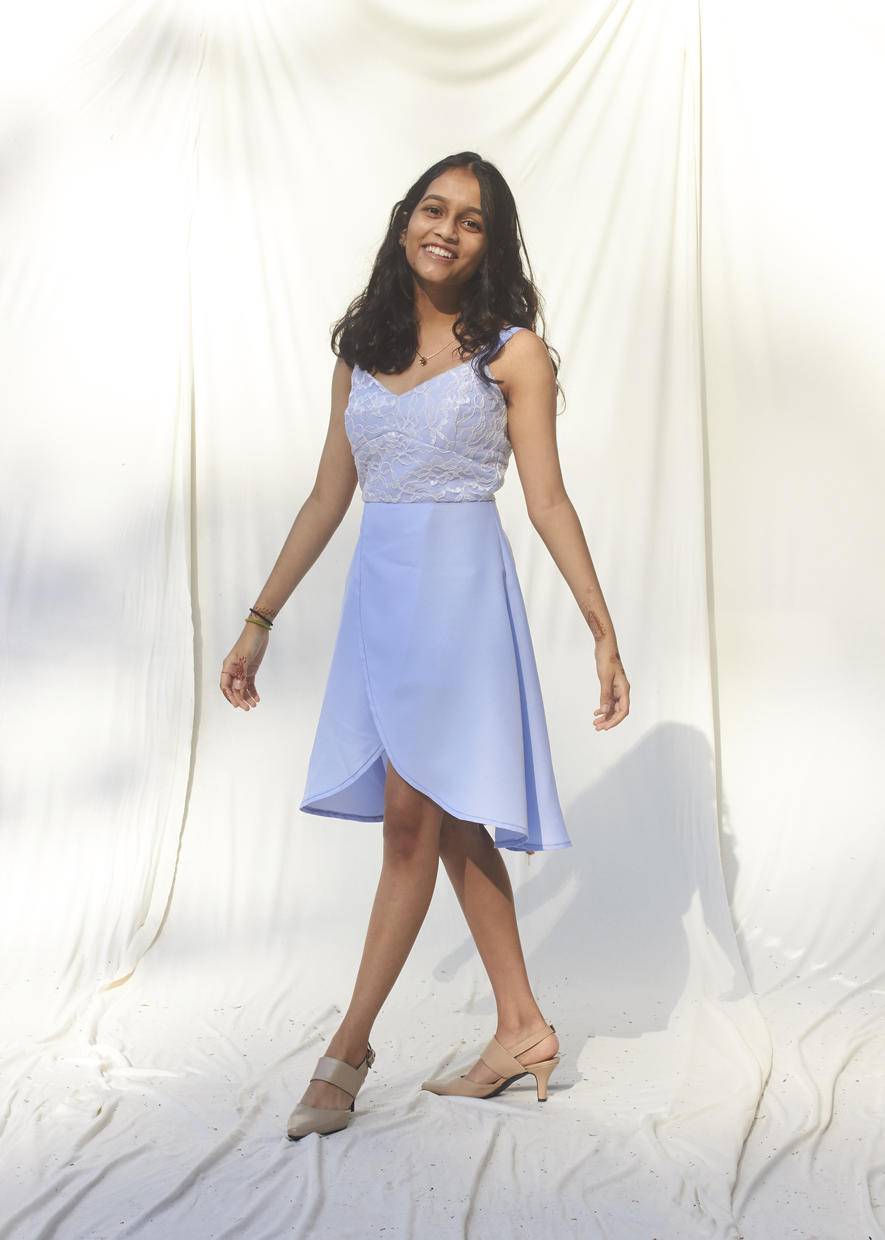  Teenage girl stands with hands out while wearing a sky blue dress with a white floral lace overlay.