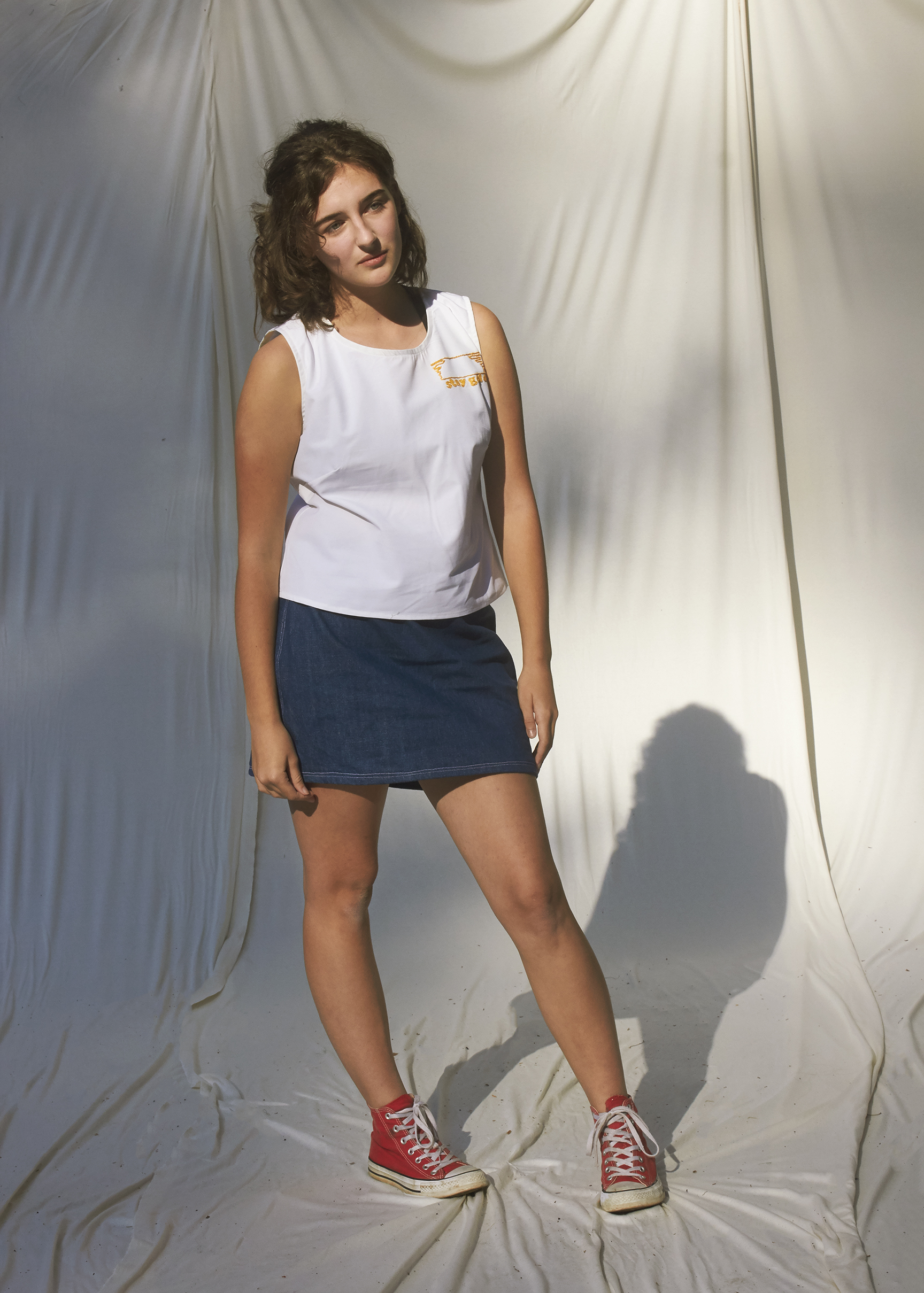 Teenage girl stands with a popped hip in a classic denim skirt and white top