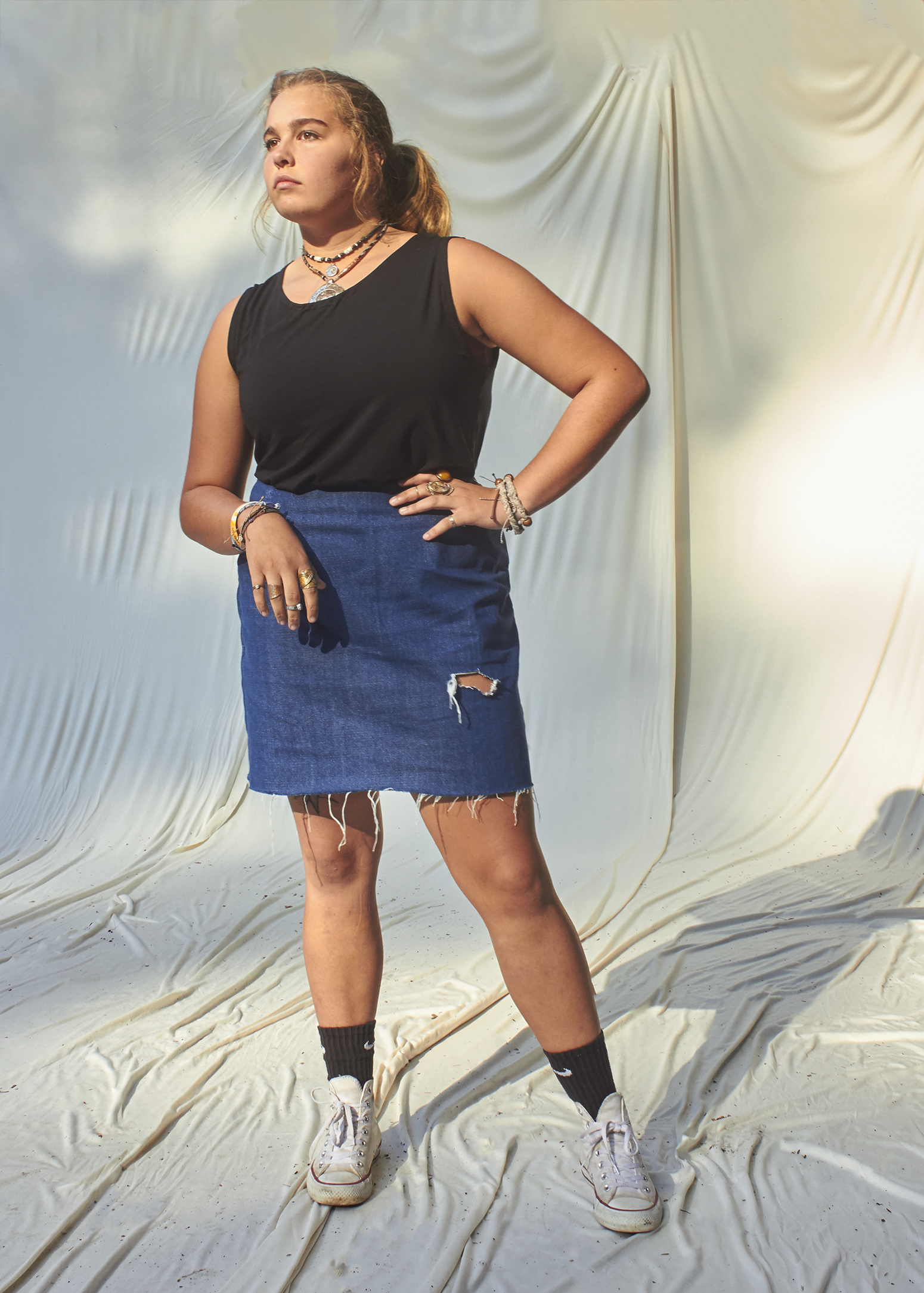 Teenage Girl standing with her hand on her hip in a black top and a denim distressed blue denim skirt.