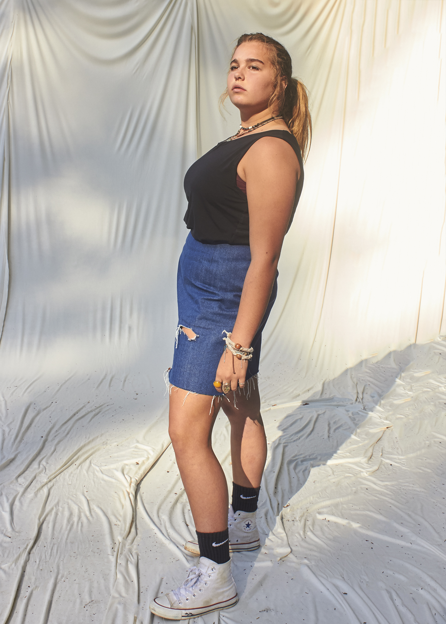 Teenage girl standing in a ripped denim mini skirt and black t-shirt.