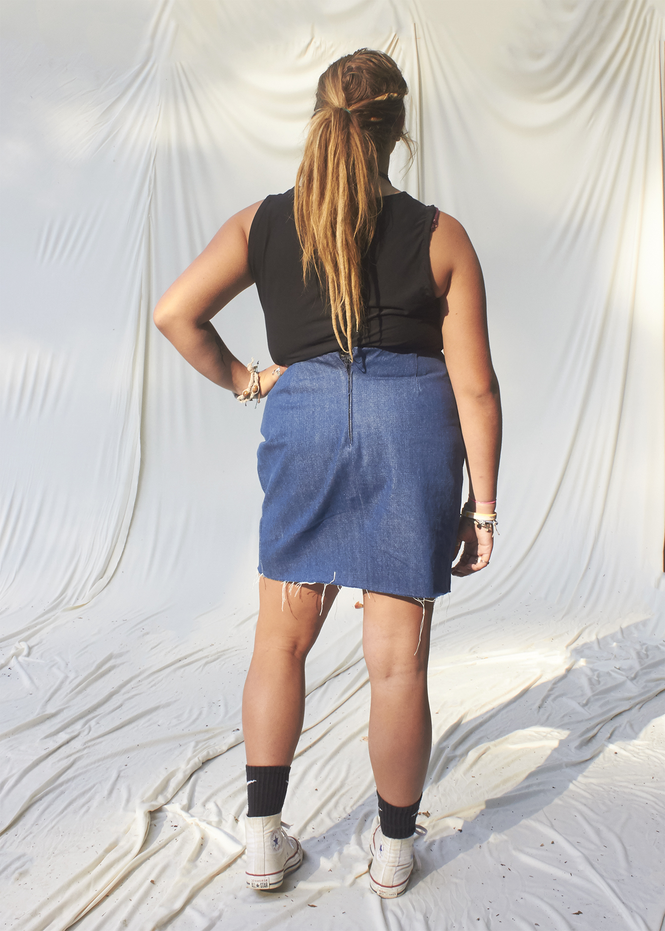 A back view of a teenage girl standing in a ripped denim mini skirt and black t-shirt.