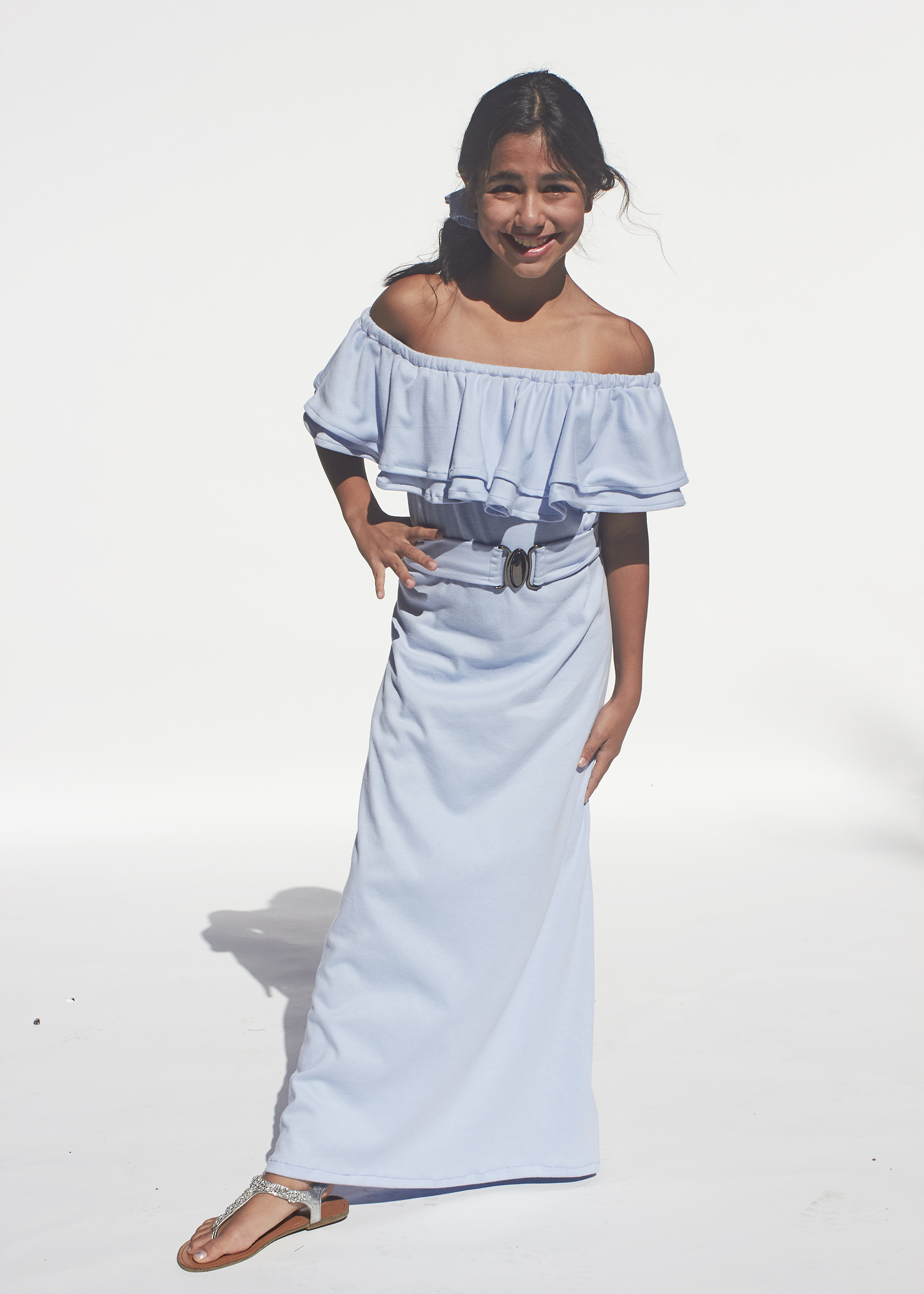 Front view of girl posing for floor length ruffled sky blue knit dress with silver buckled belt