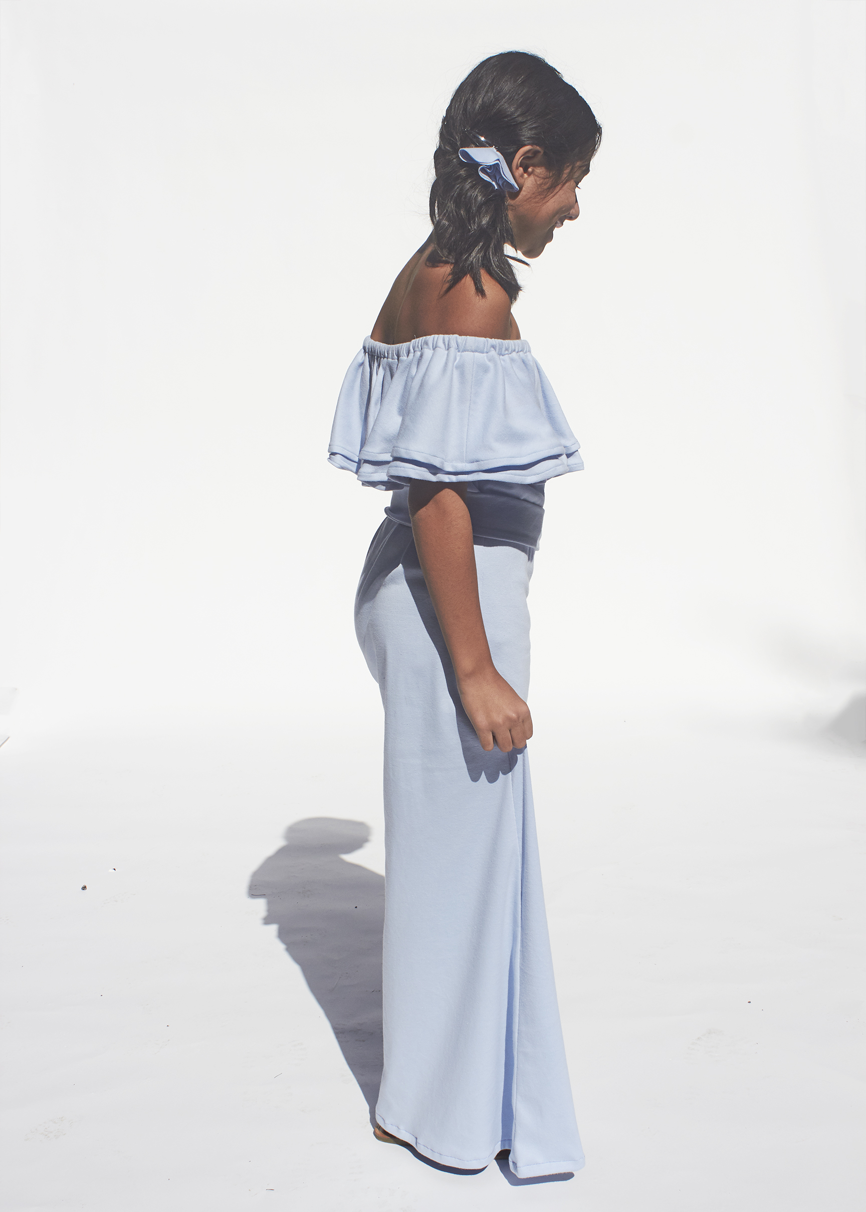 side view of girl posing for floor length ruffled sky blue knit dress with silver buckled belt