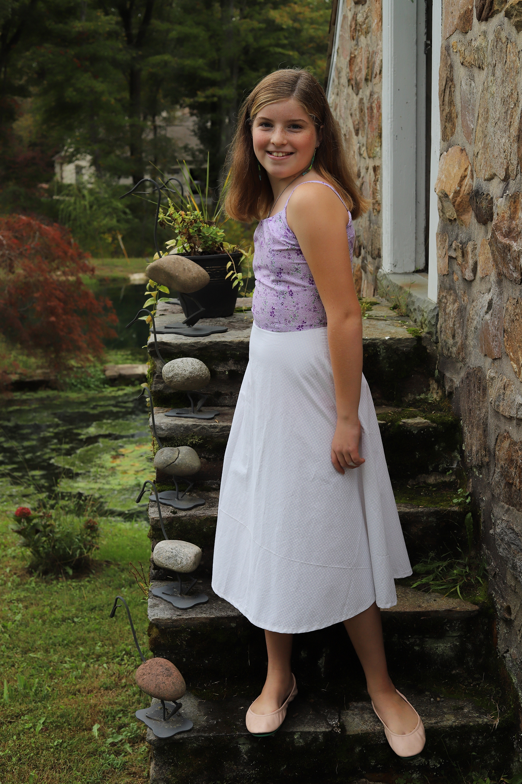 Girl standing in 50s style purple and white dress in a garden