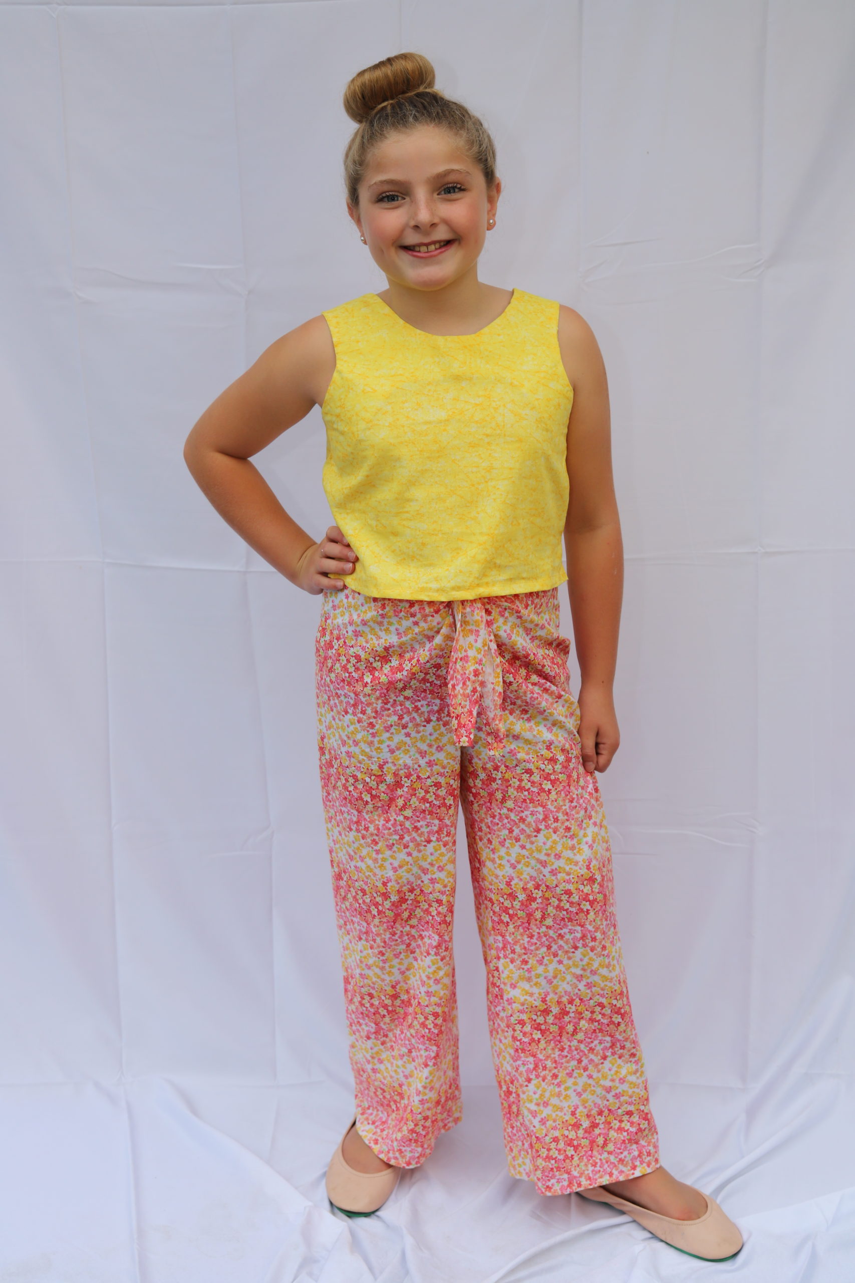 Girl standing in bright yellow top and light pink and yellow pants