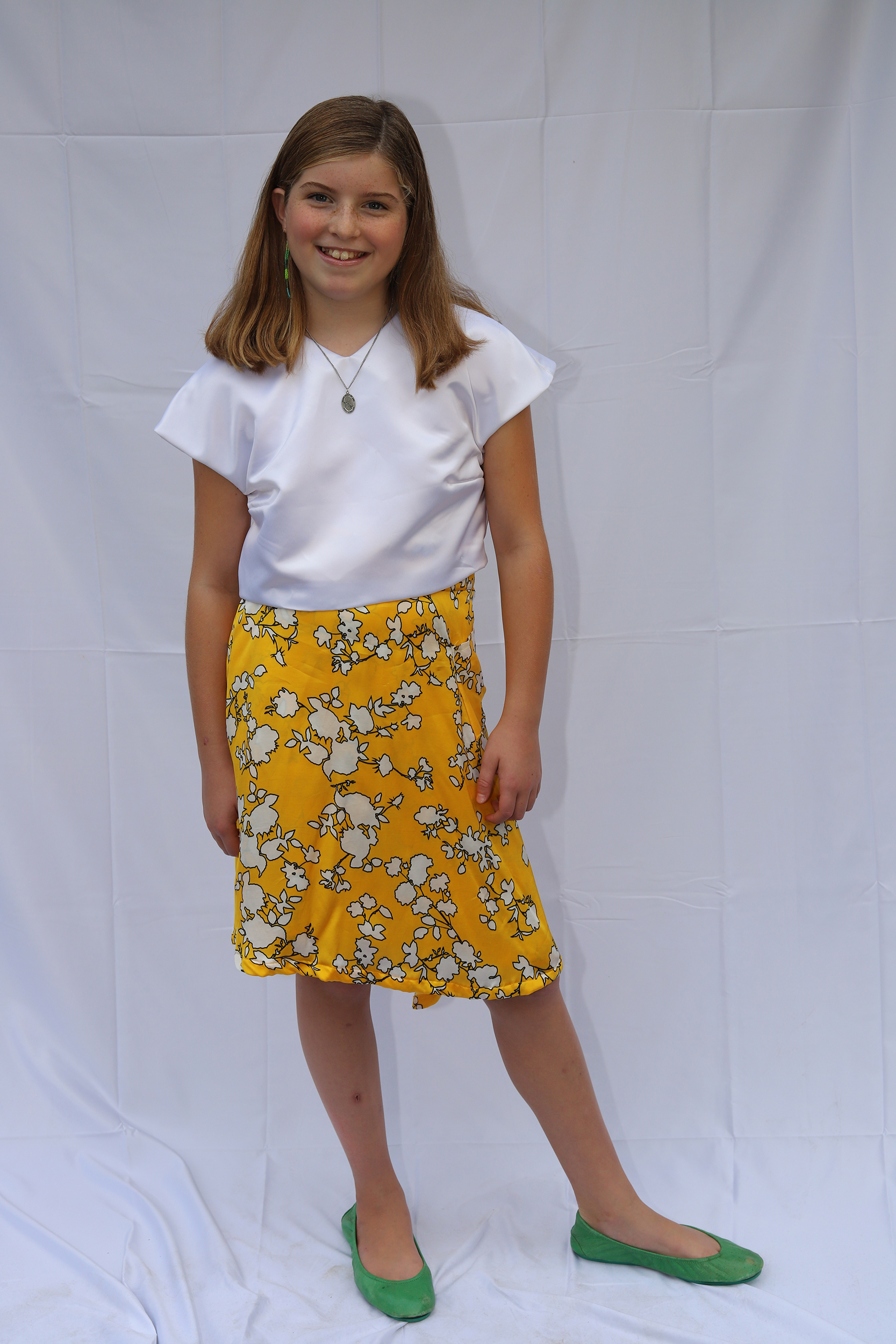 Girl standing I white tailored top and yellow floral skirt