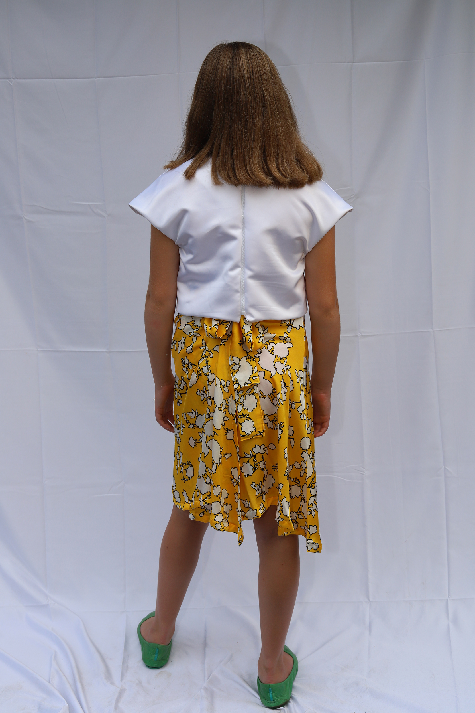 Back view of girl posing in white top and yellow floral skirt