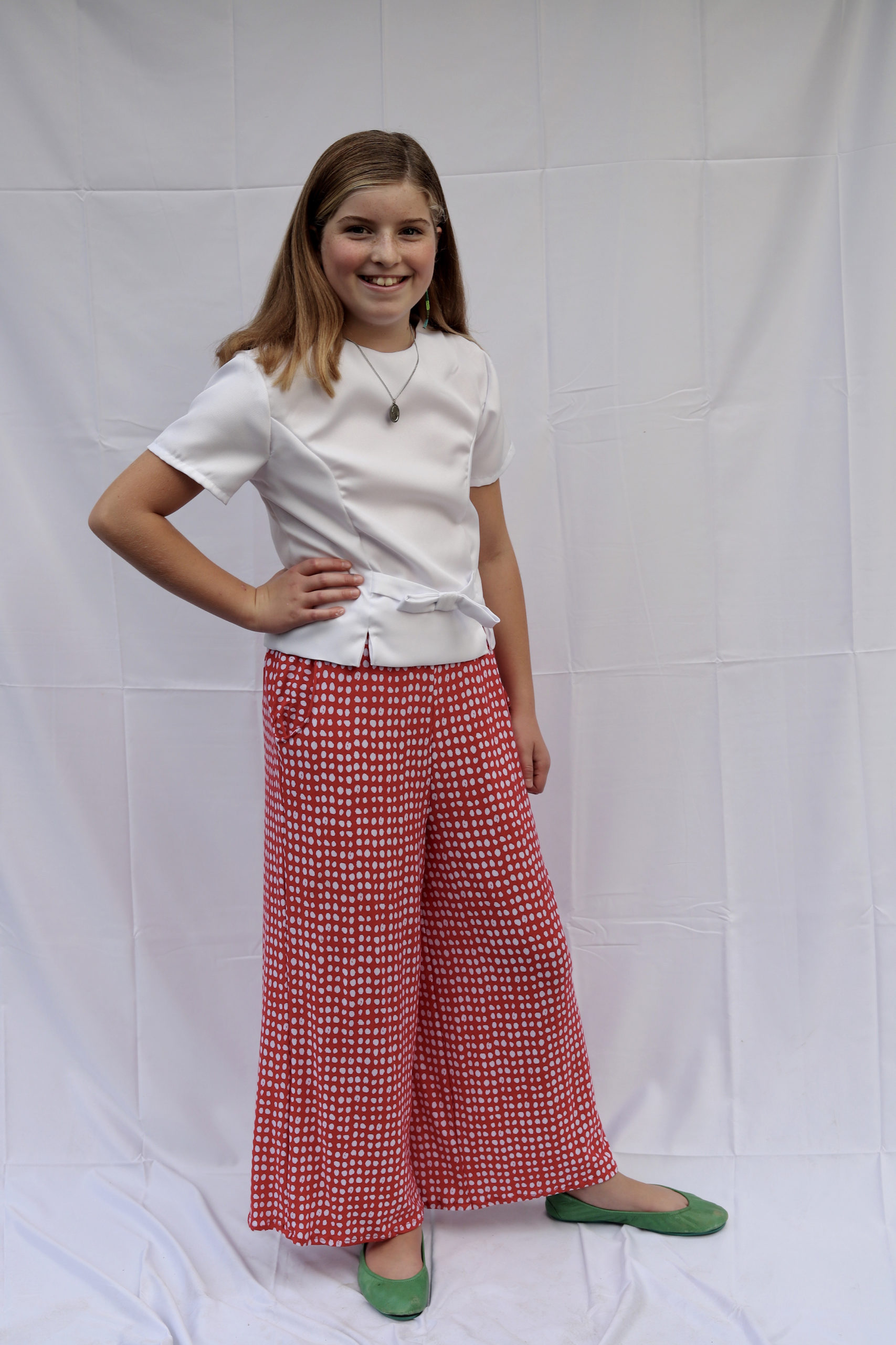 Girl standing in red polka dot knit pants and vintage white top with bow