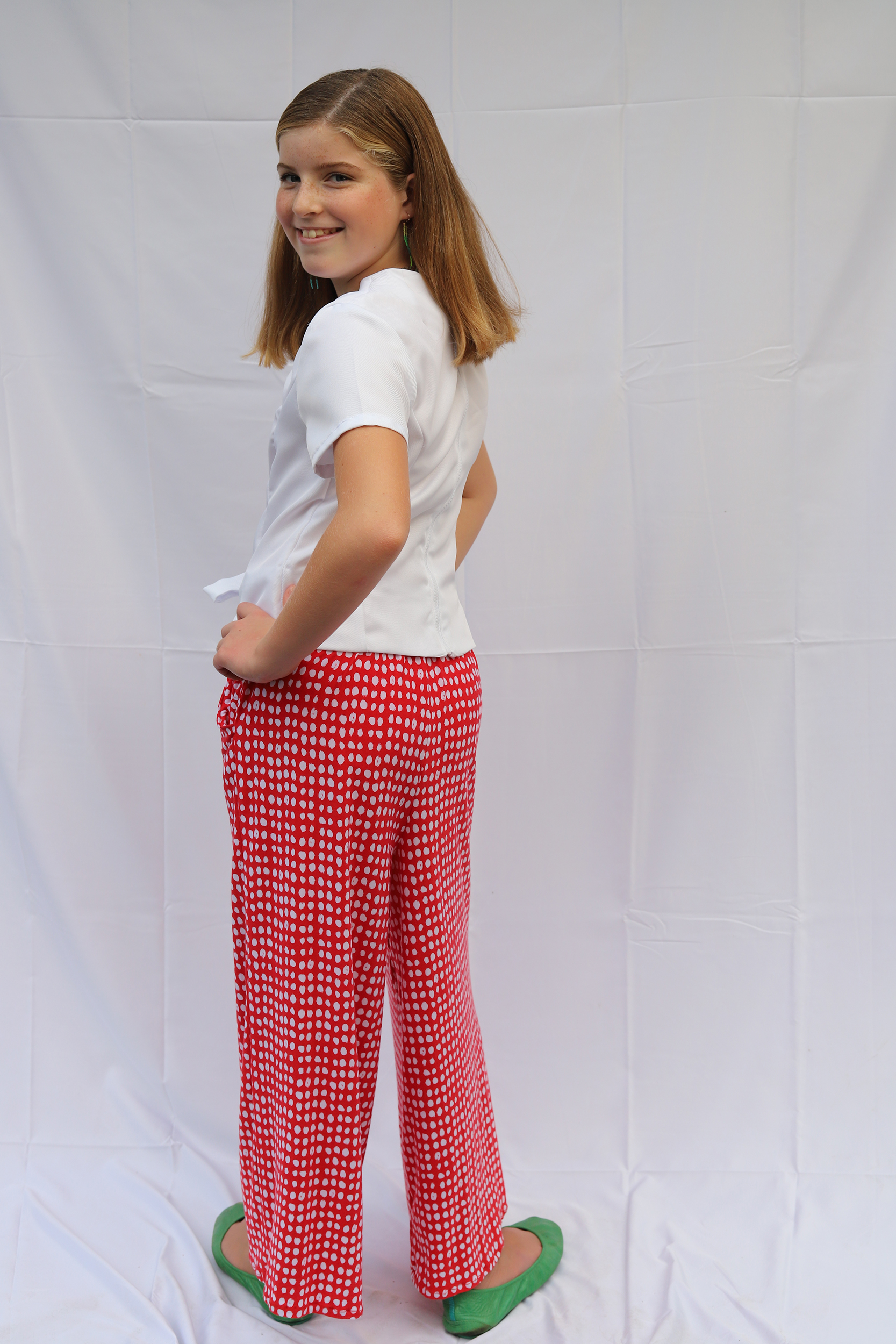 Back view of girl standing in red polka dot knit pants and vintage white top with bow