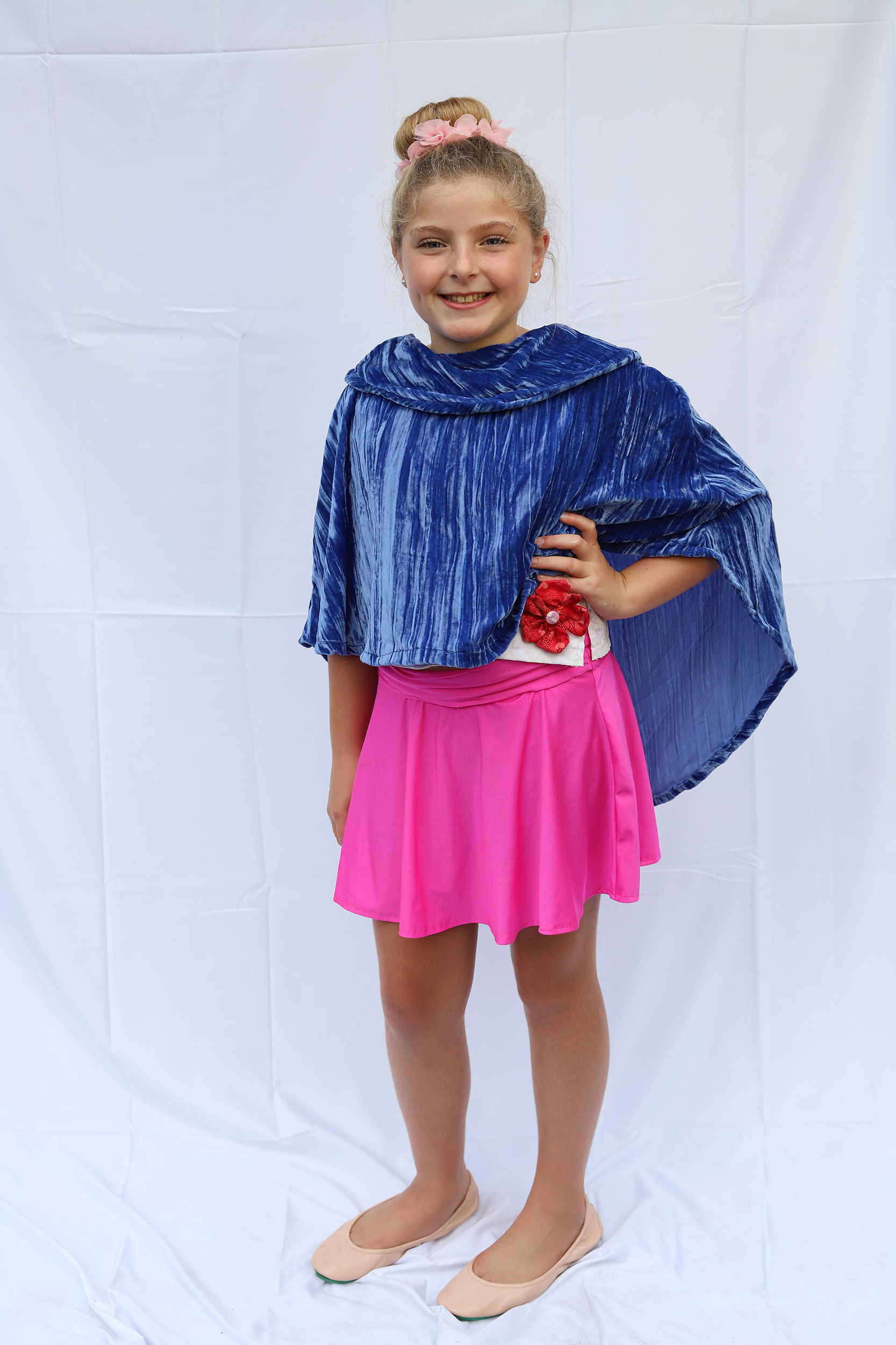 Girl standing in blue velvet cape and hot pink skirt with her hand on her hip