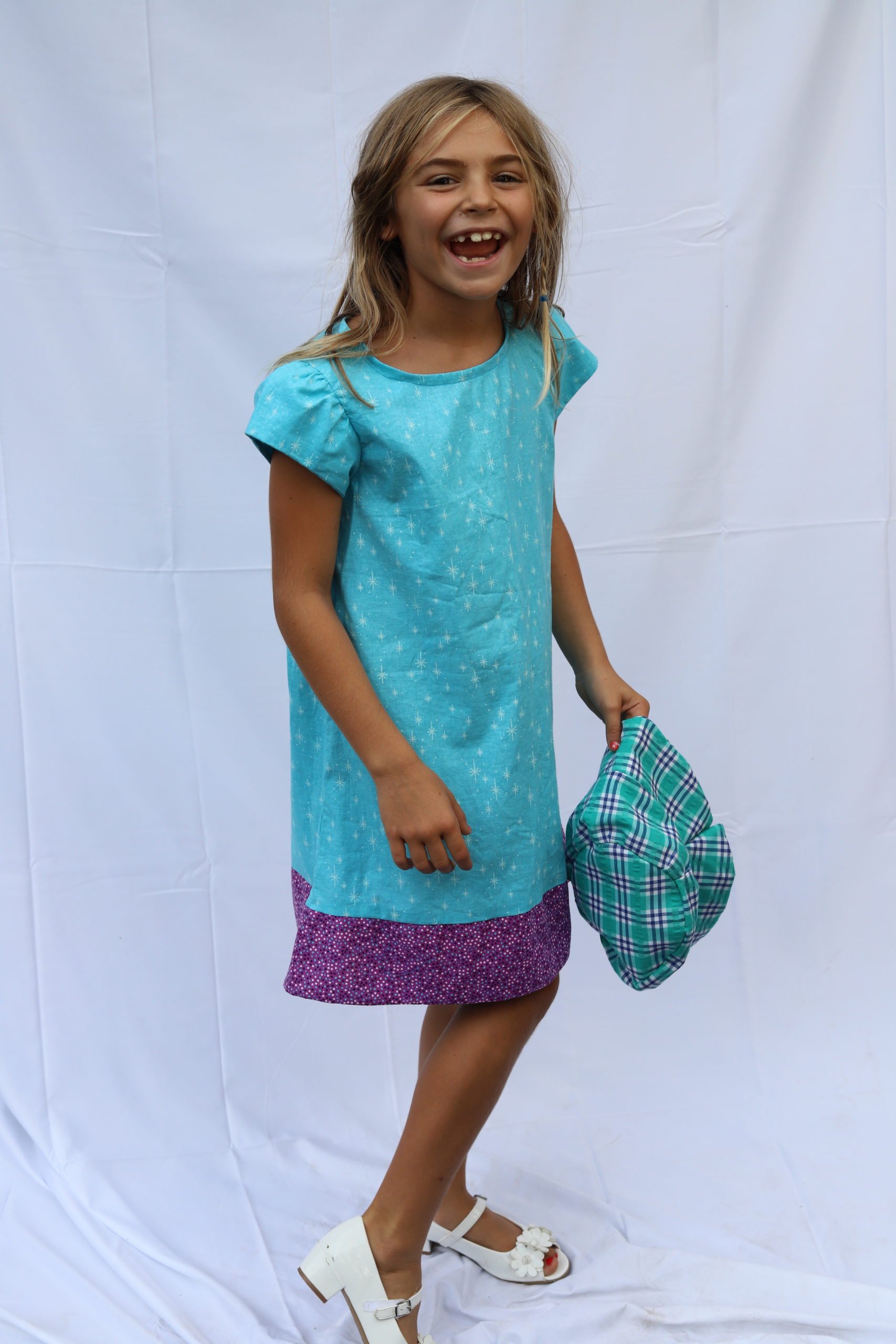 Smiling girl in aqua dress with plaid bucket hat in hand