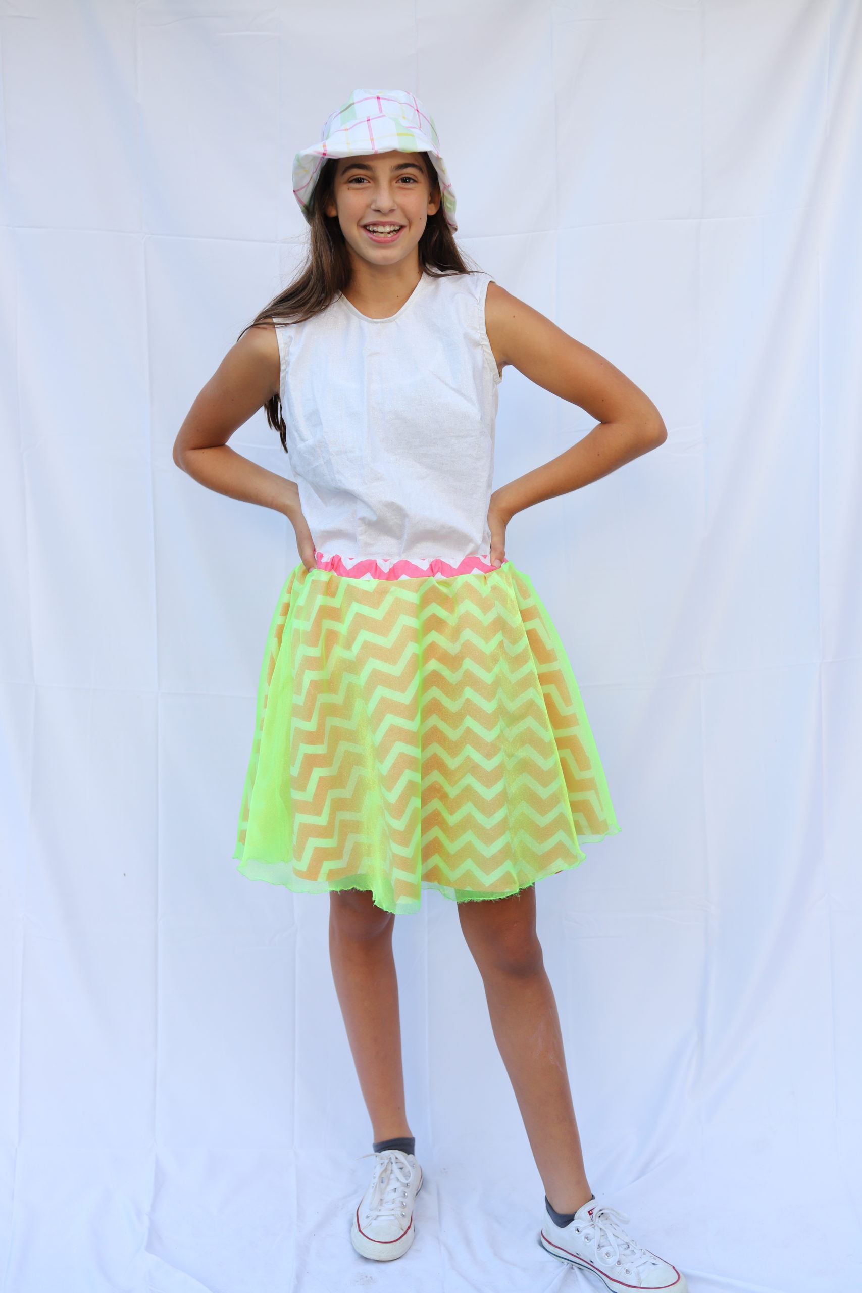 Girl stand in plaid bucket hat, white top, and neon yellow skater skirt