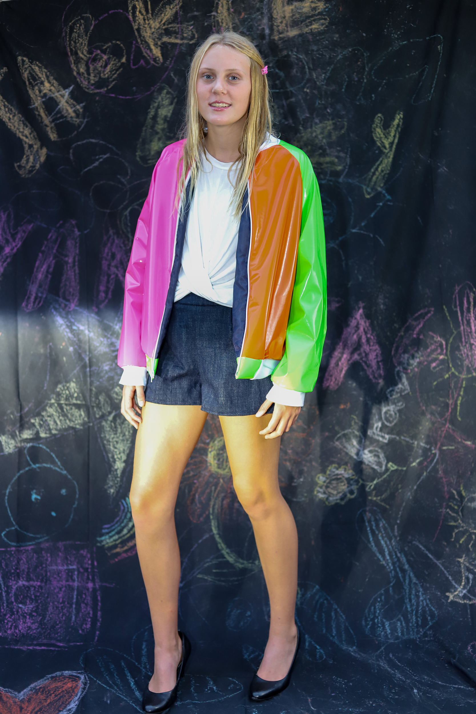 Girl standing in neon bomber jacket and denim shorts