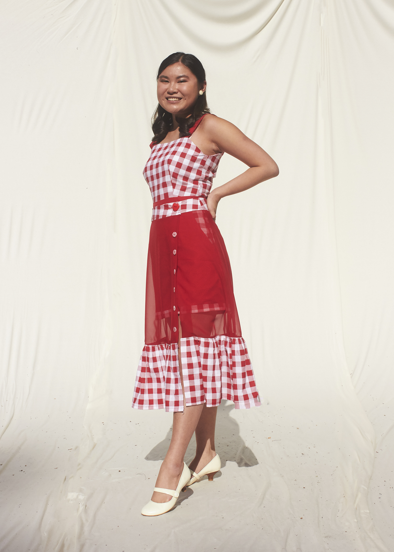 Girl stands in a gingham red romper and a sheer red frilly skirt