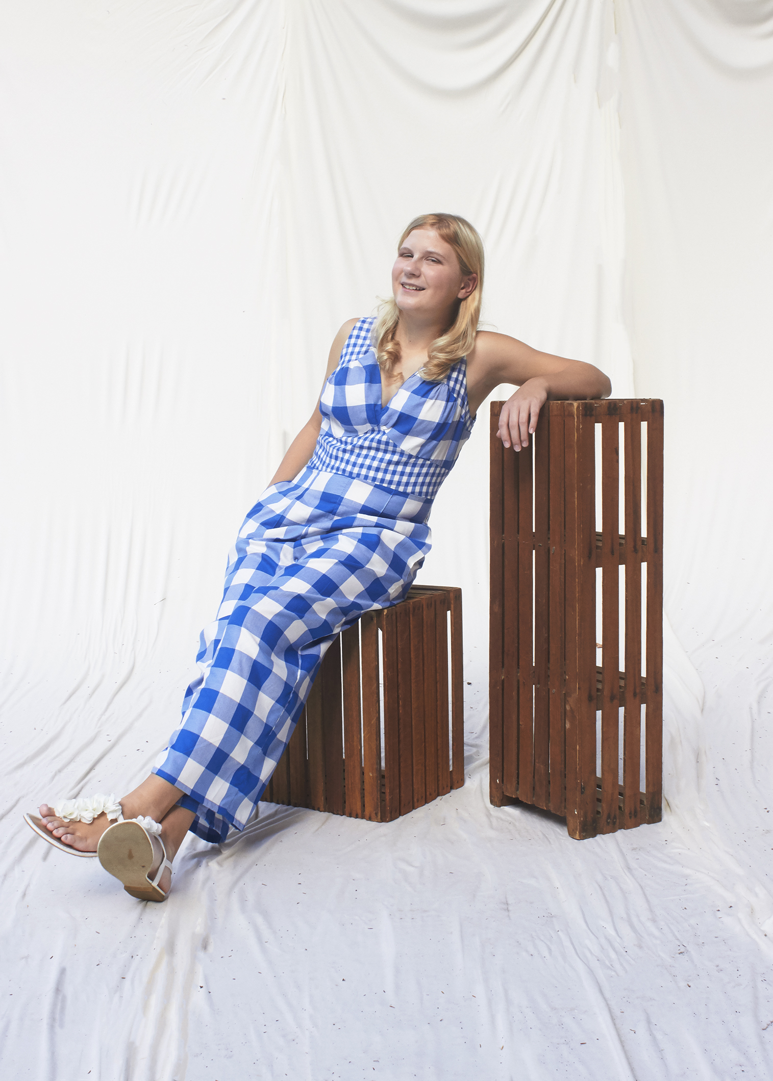 Girl sitting on crates in a blue gingham jumpsuit