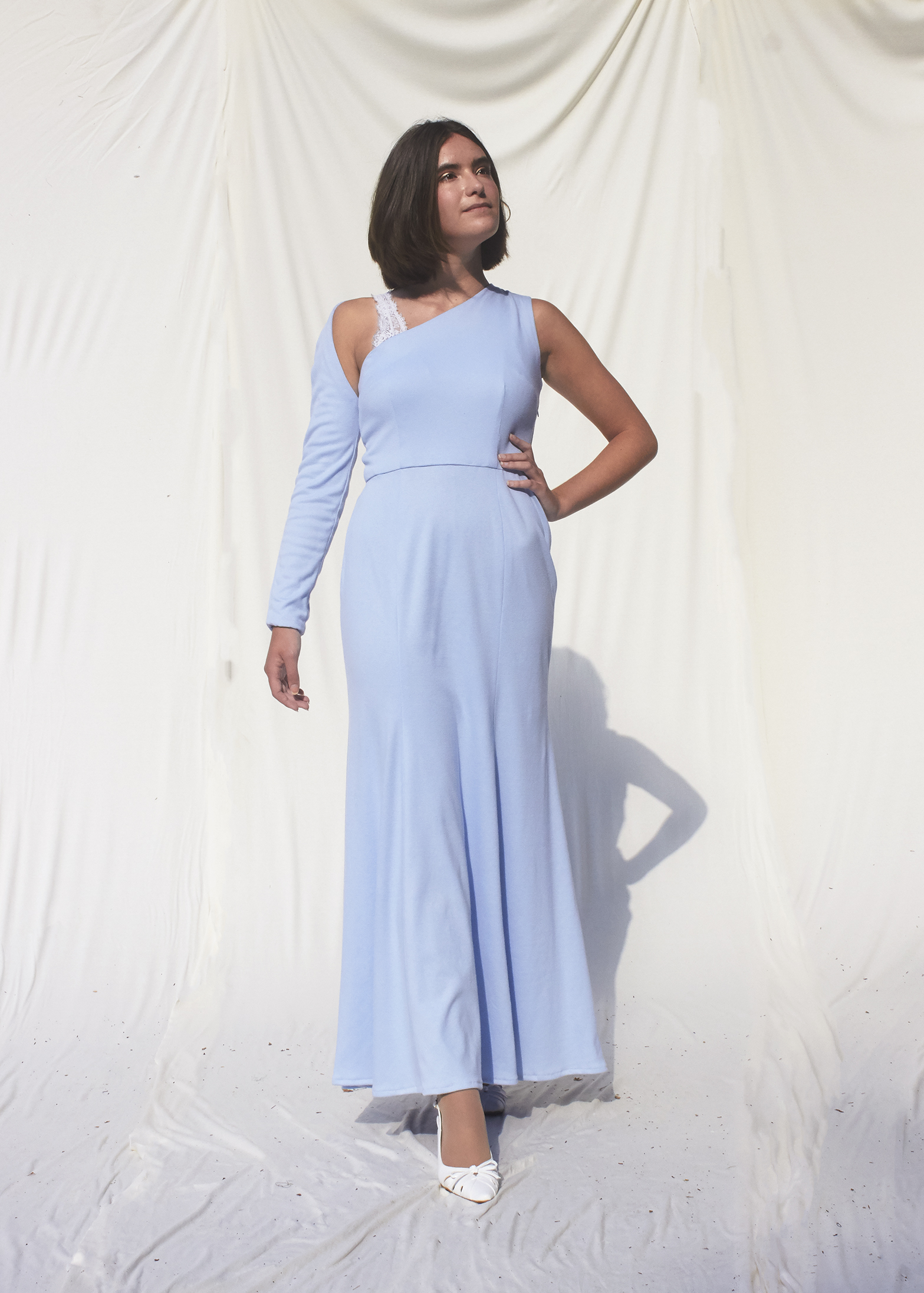 Girl posing in asymmetrical sky blue knit gown wit one long sleeve