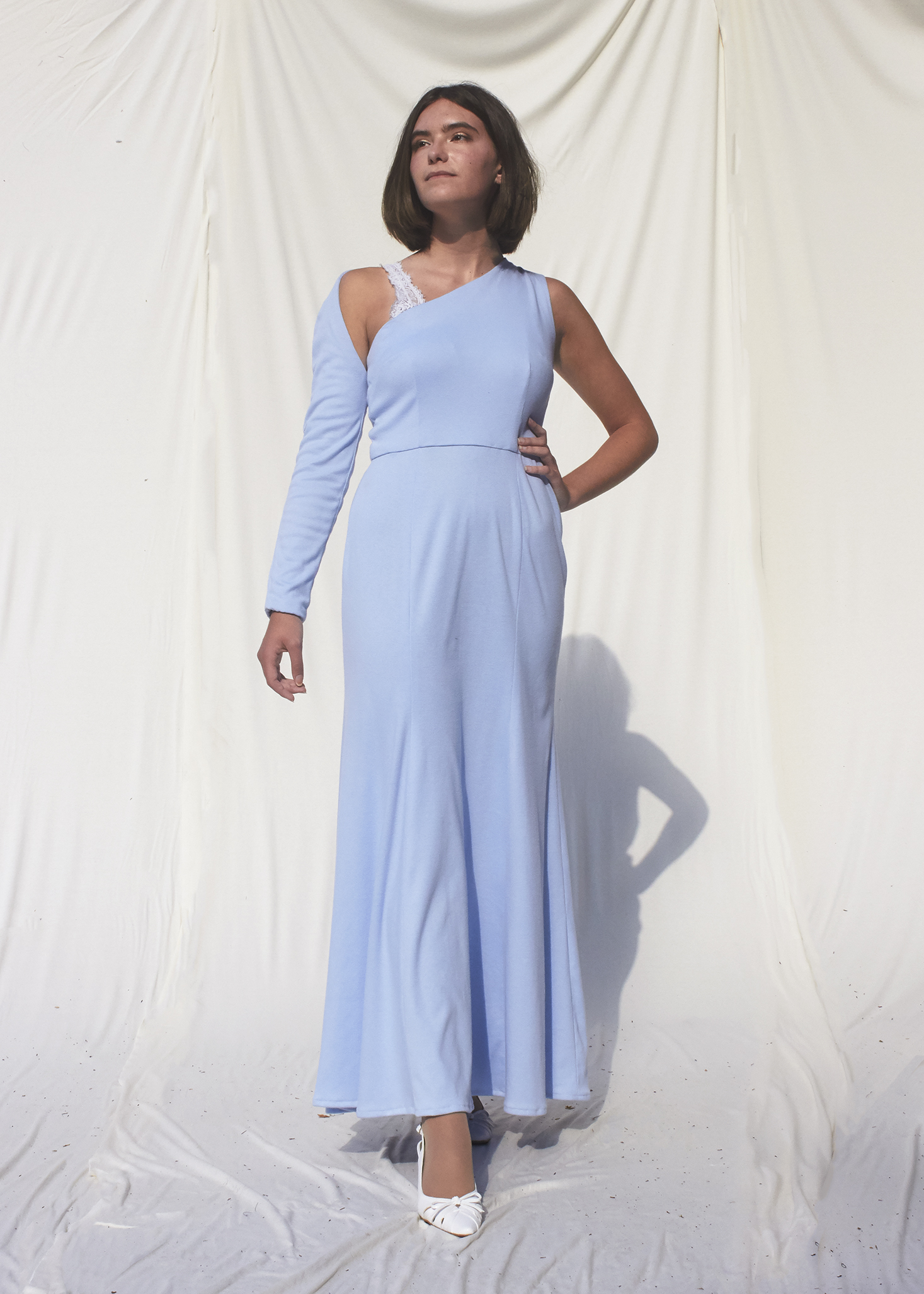 Girl poses in asymmetrical sky blue knit gown wit one long sleeve