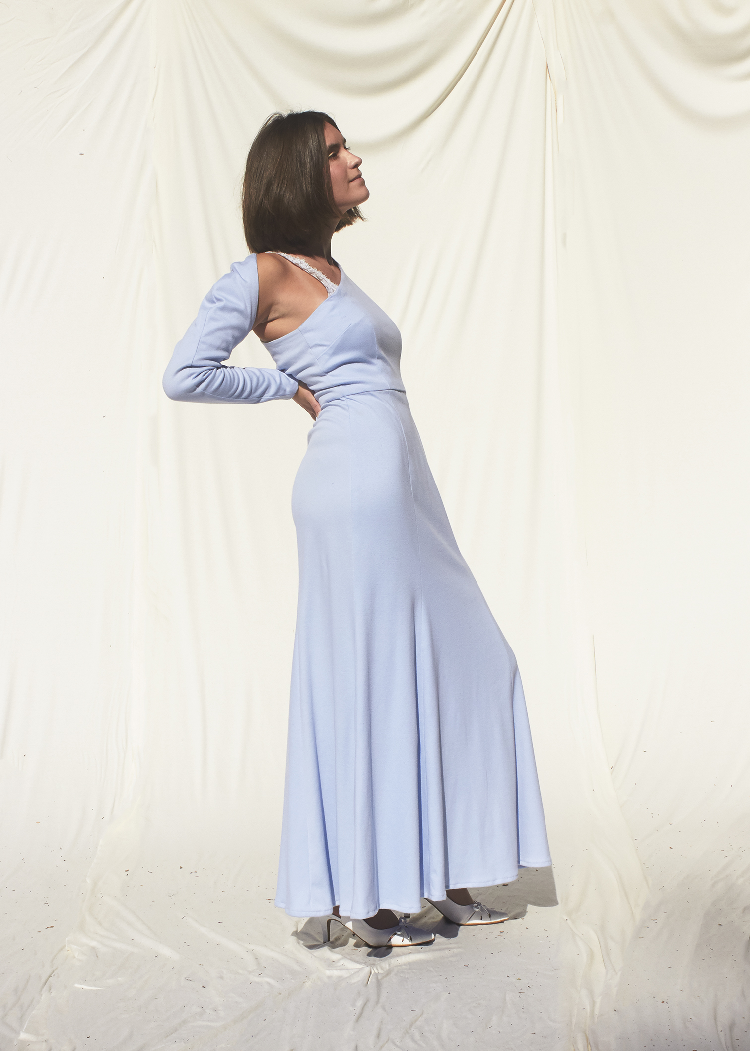 Side view of girl posing in asymmetrical sky blue knit gown wit one long sleeve