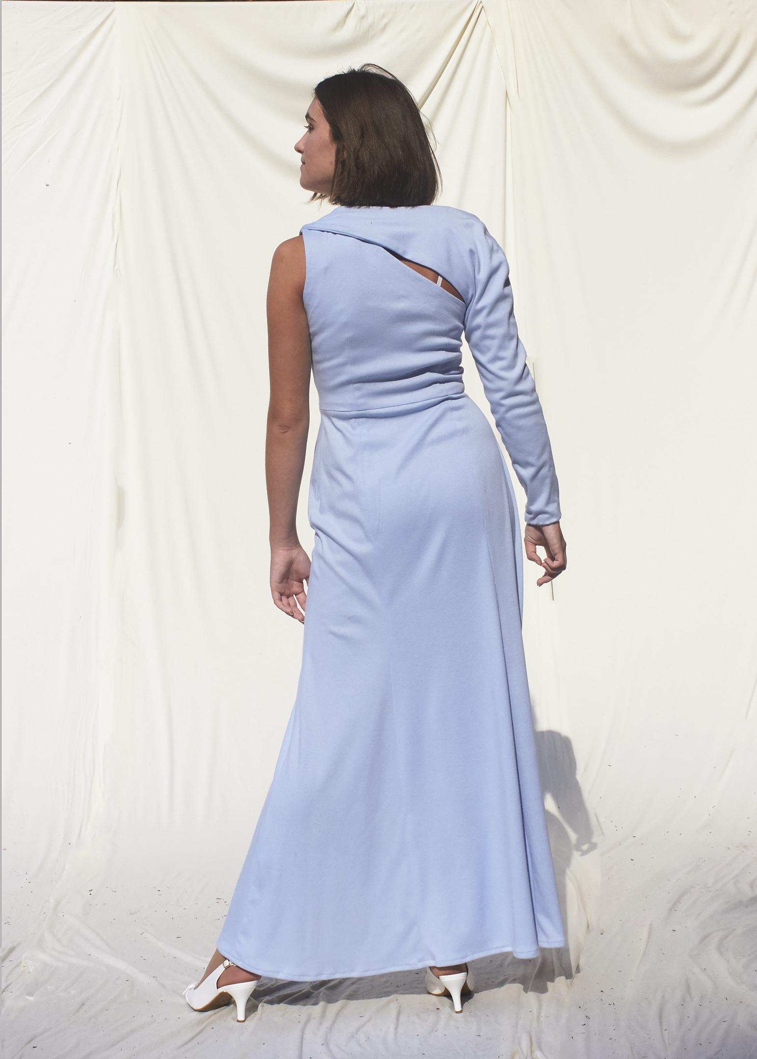 Back view of Girl posing in asymmetrical sky blue knit gown wit one long sleeve