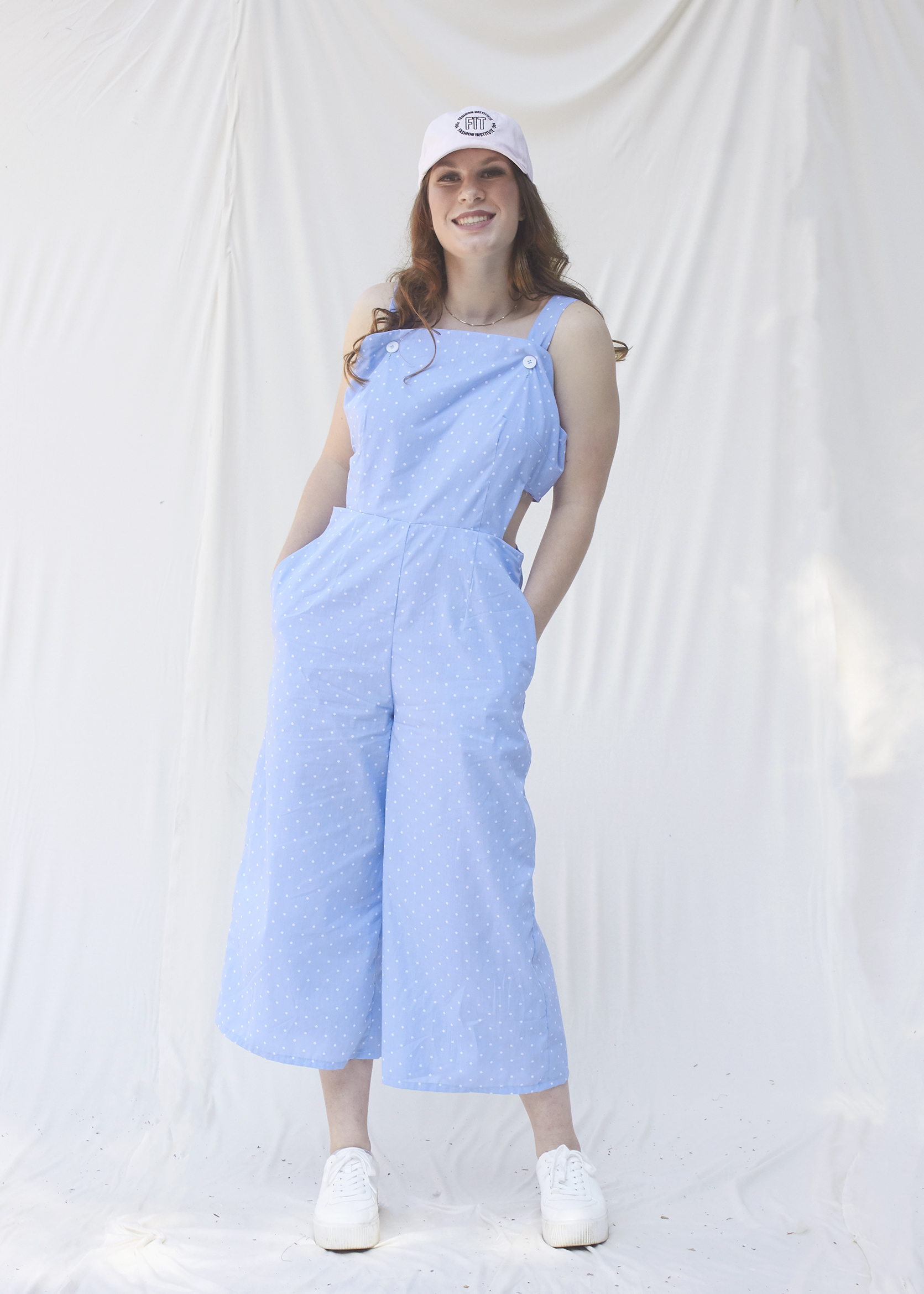 Teenage girl stands leaning to the right in a light blue cut out jumpsuit