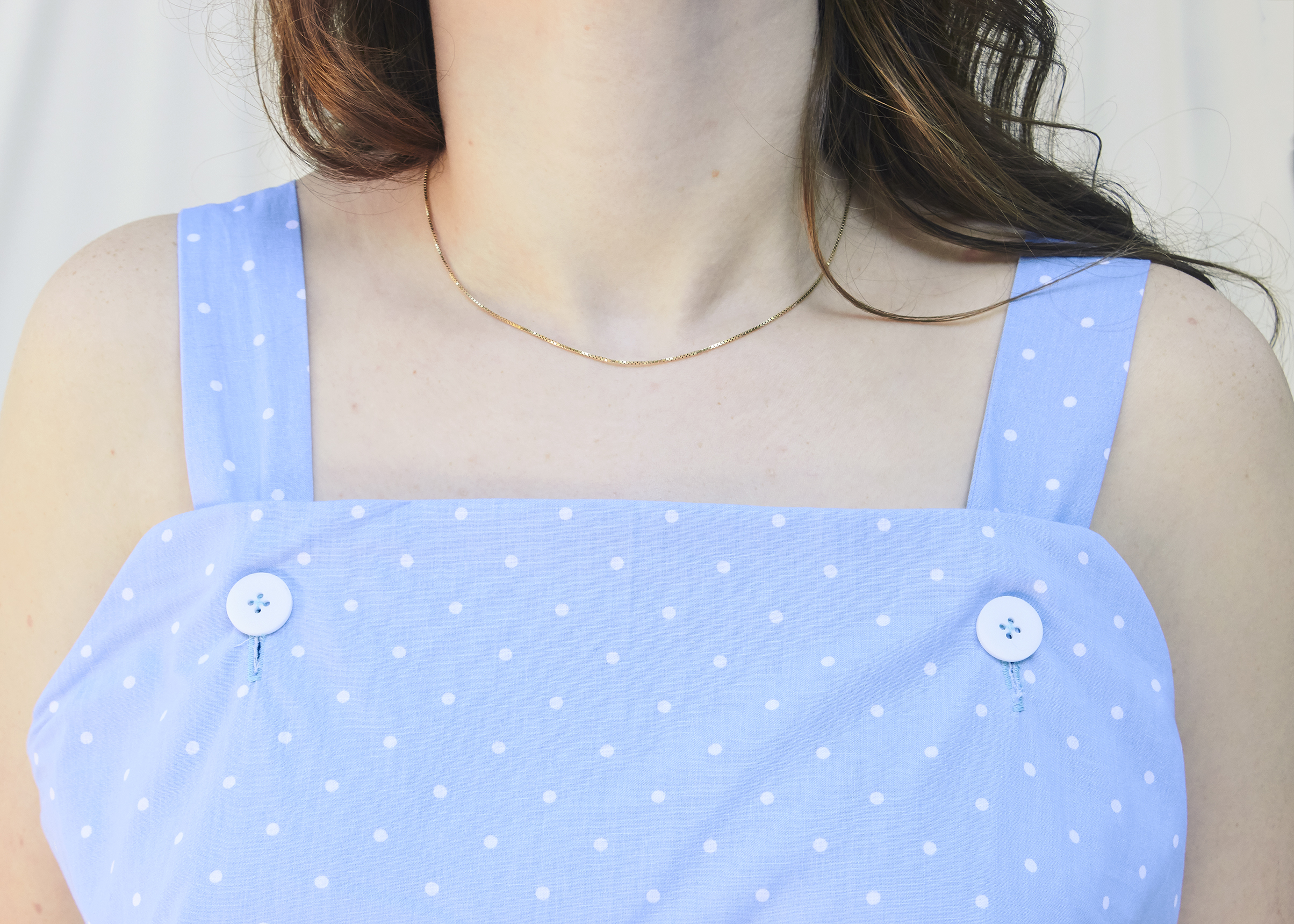 Close up view of a button detail on a strap of a light blue jumpsuit