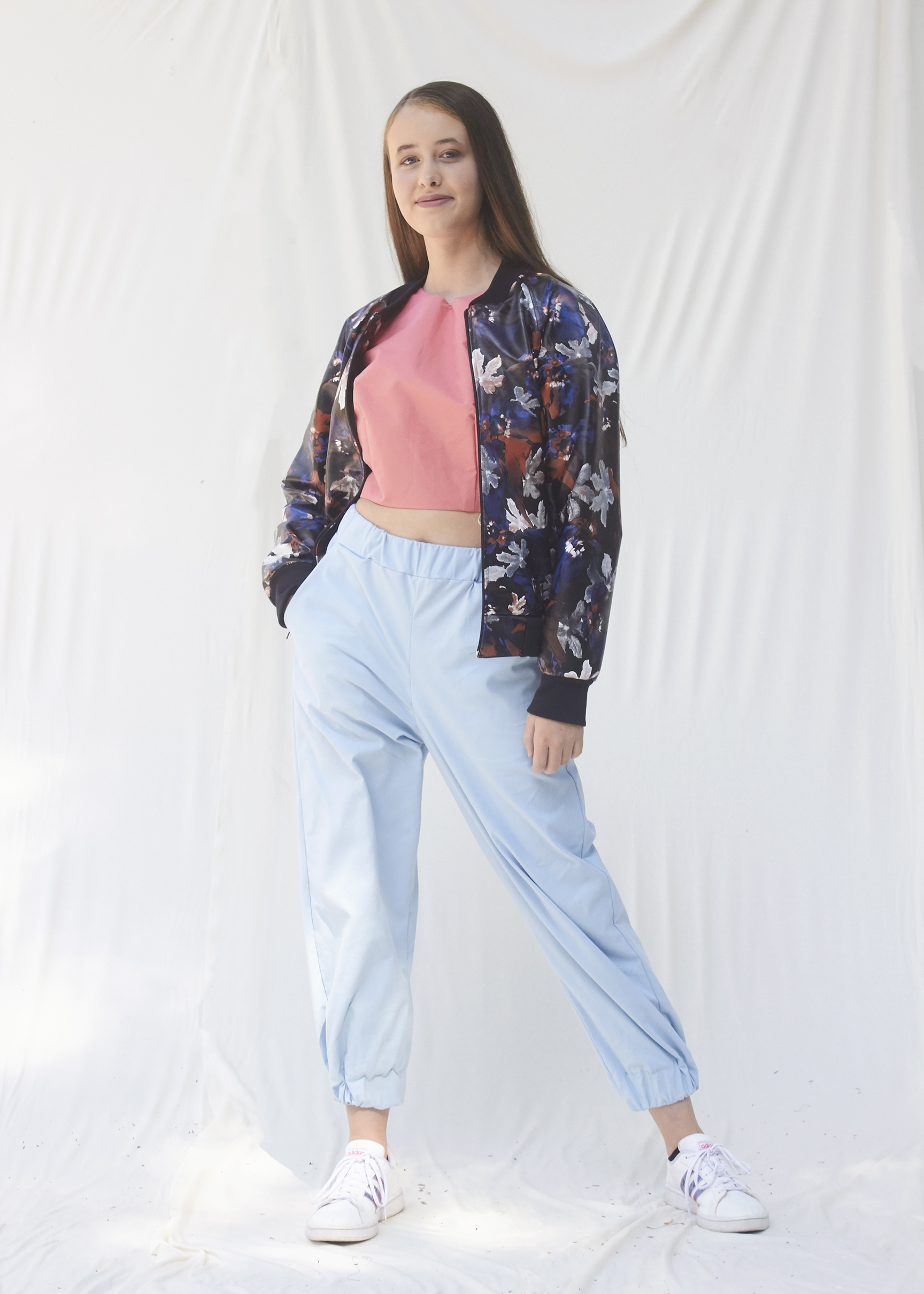 Photo of a girl posing in light blue pants and pink top with a pleather floral bomber jacket