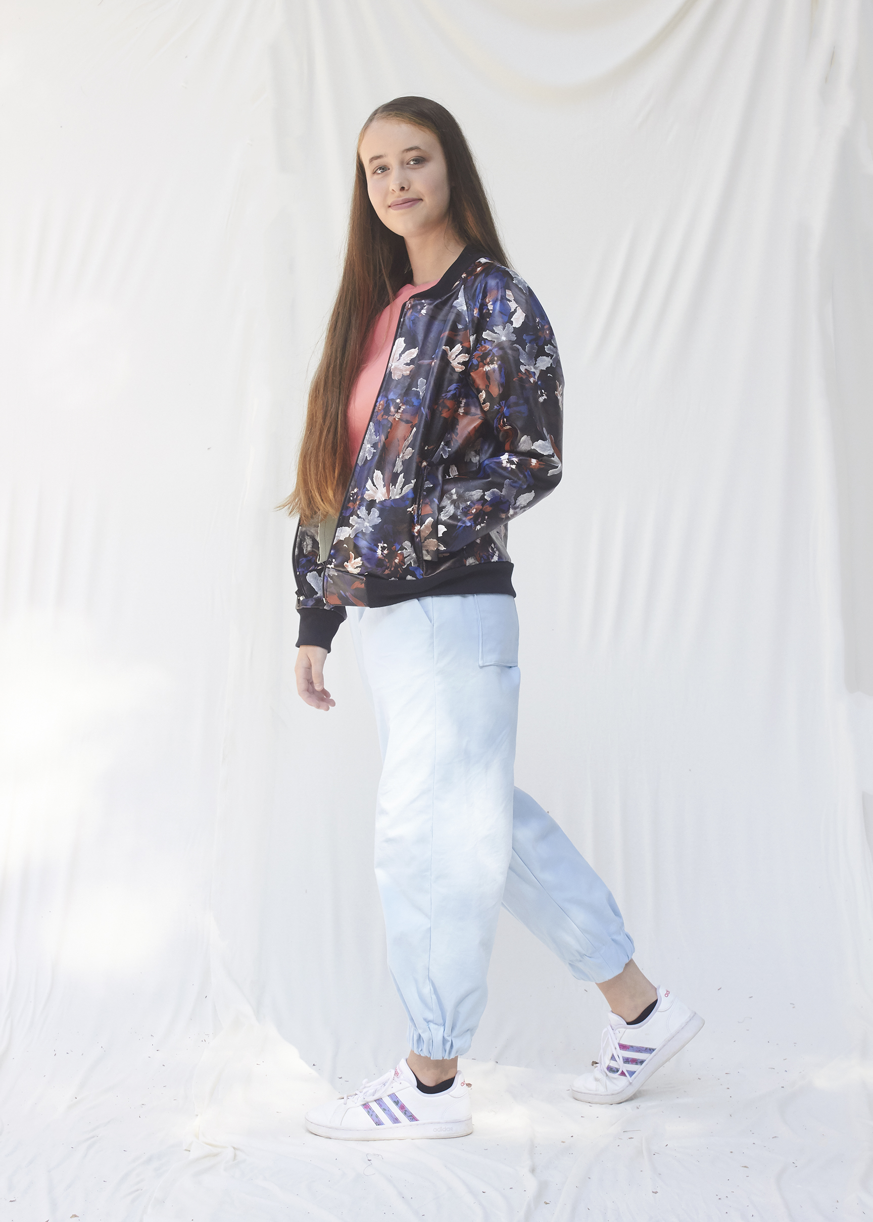 Side view of a girl posing in a pleather bomber jacket and light blue cargo shorts