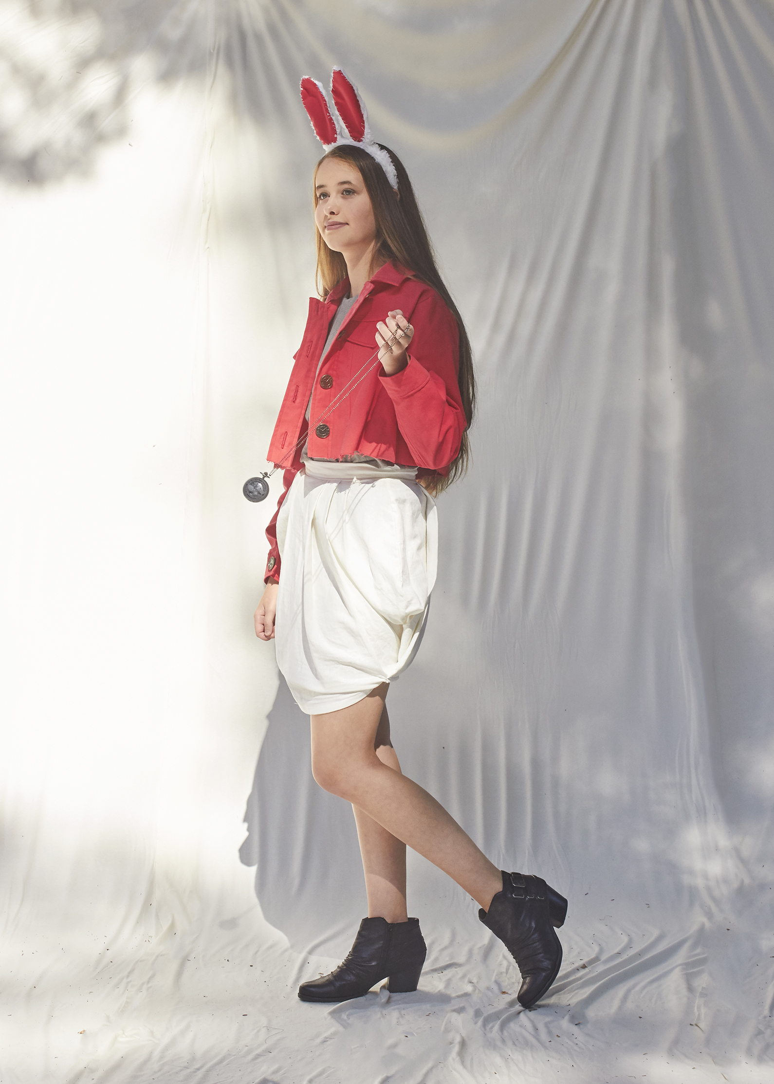 Girl standing in shite draped skirt and cropped red denim jacket and posing as the white rabbit for Alice and Wonderland 