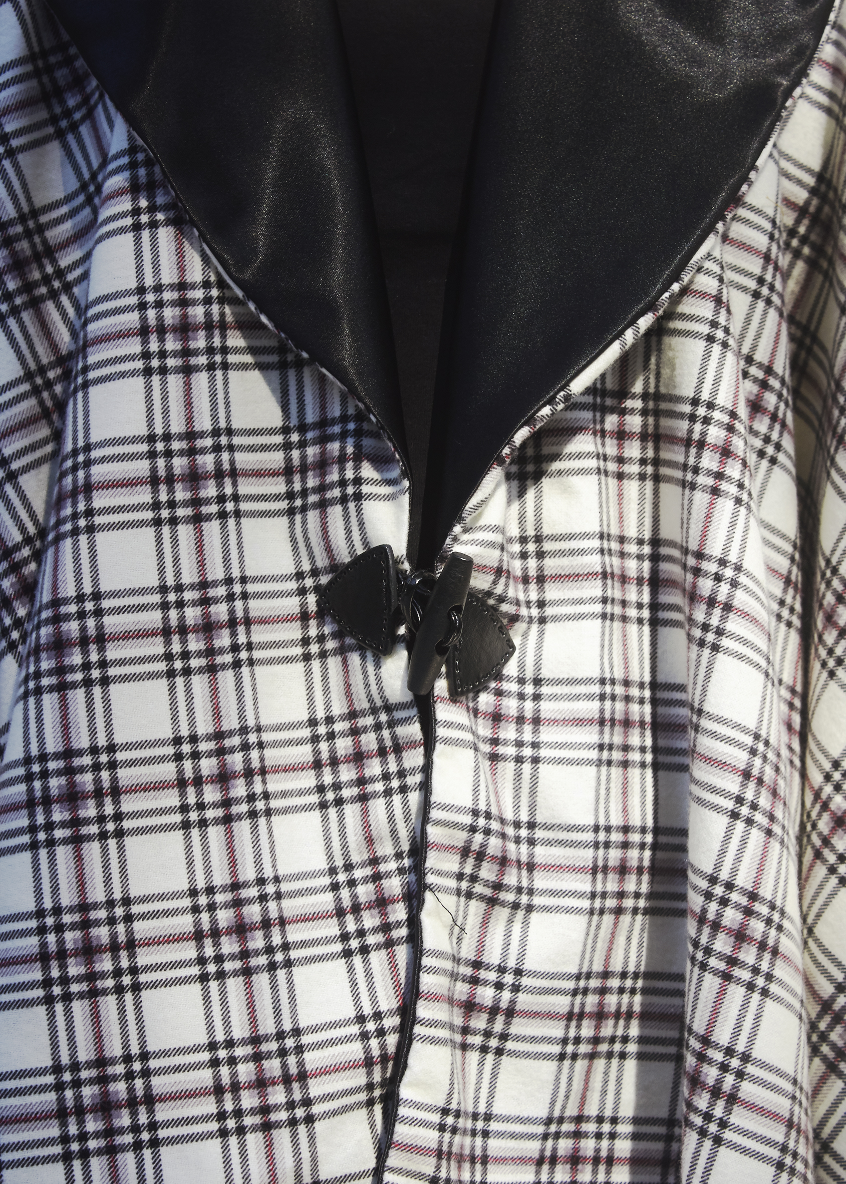 Close up photo of a black and white plaid poncho with a black hook closure