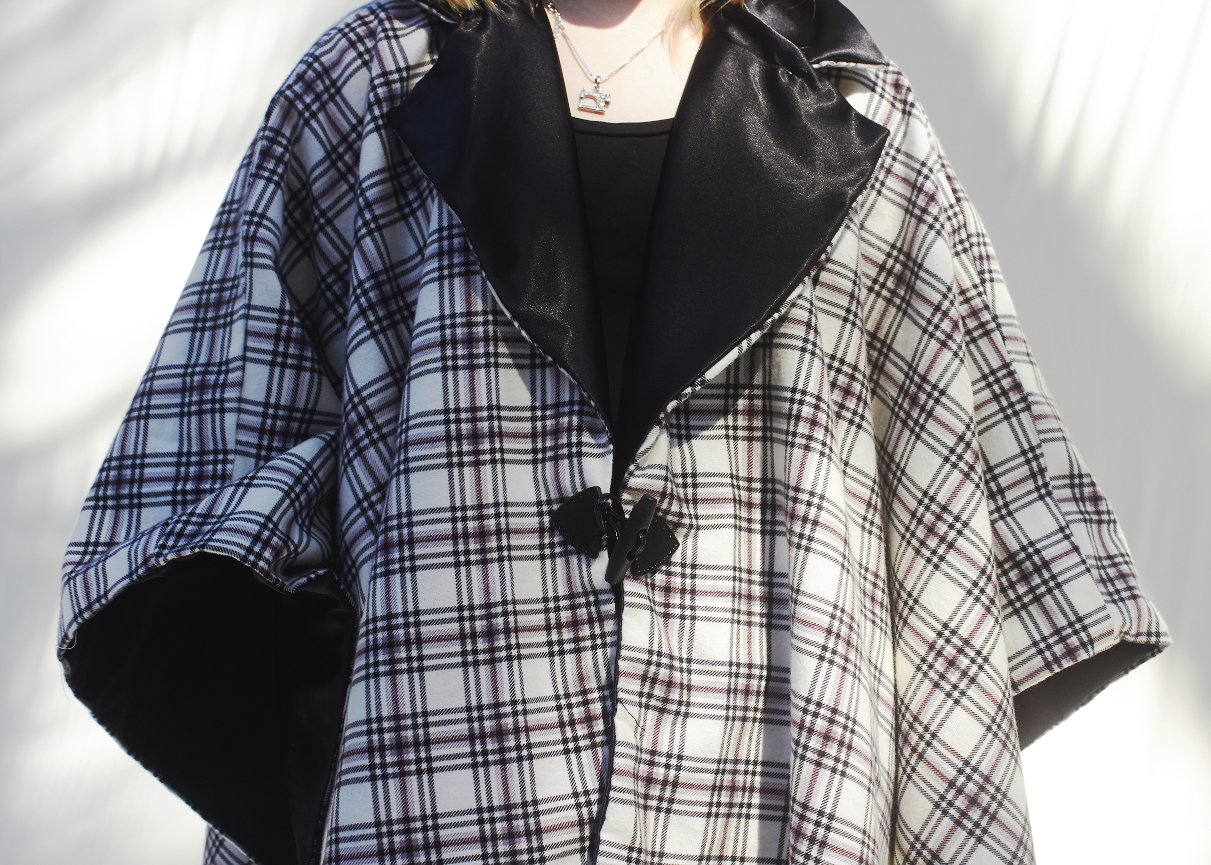 Close up photo of a black and white plaid poncho with a satin collar