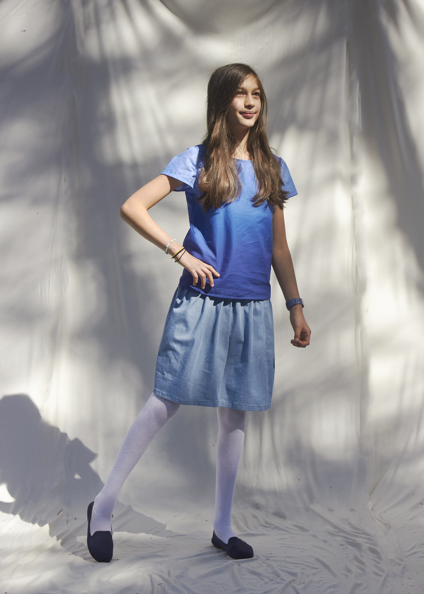 Young girl stand in a spring time outfit in a ombre blue top and a sky blue skirt with her hand on her hip