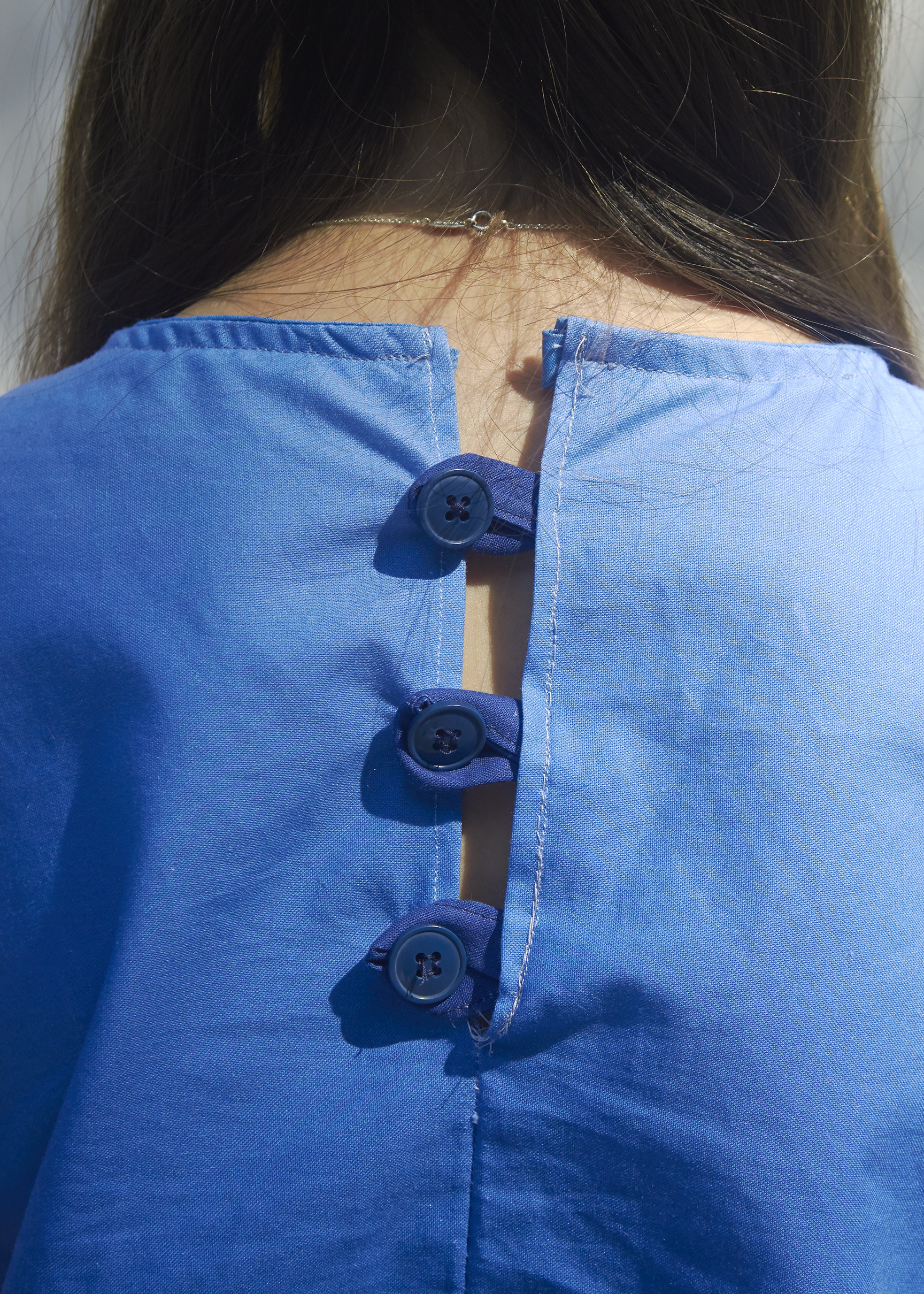 Close up view of an ombre blue short sleeve shirt with three blue buttons in the back