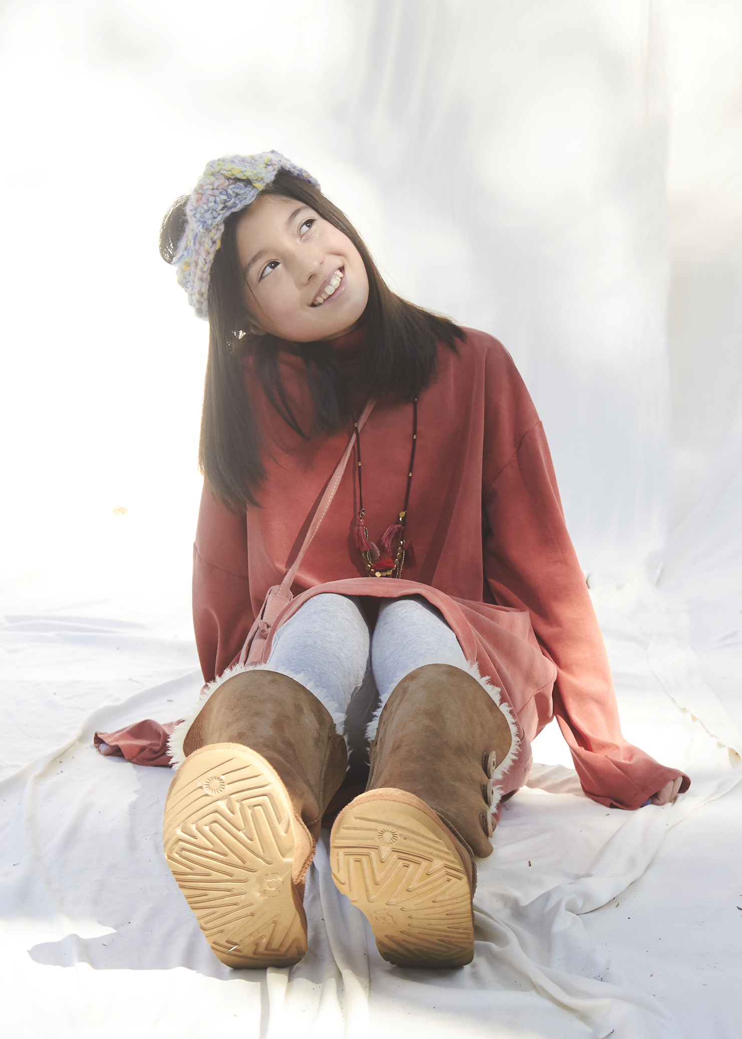 Young Girl sitting in a burnt orange sweater dress and uggs