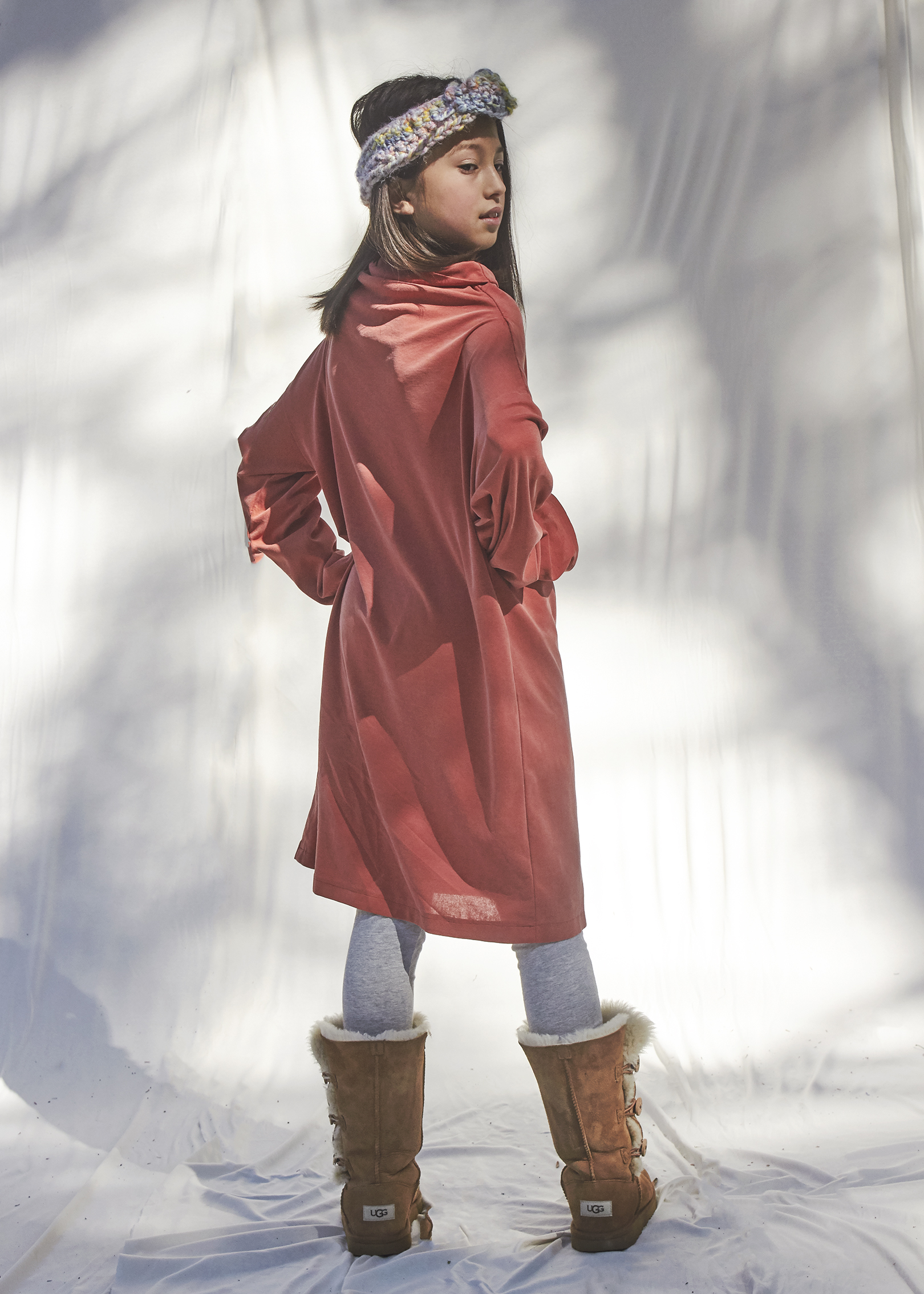 Girl standing look over her shoulder at the camera. She is wearing a rust color long sweater dress