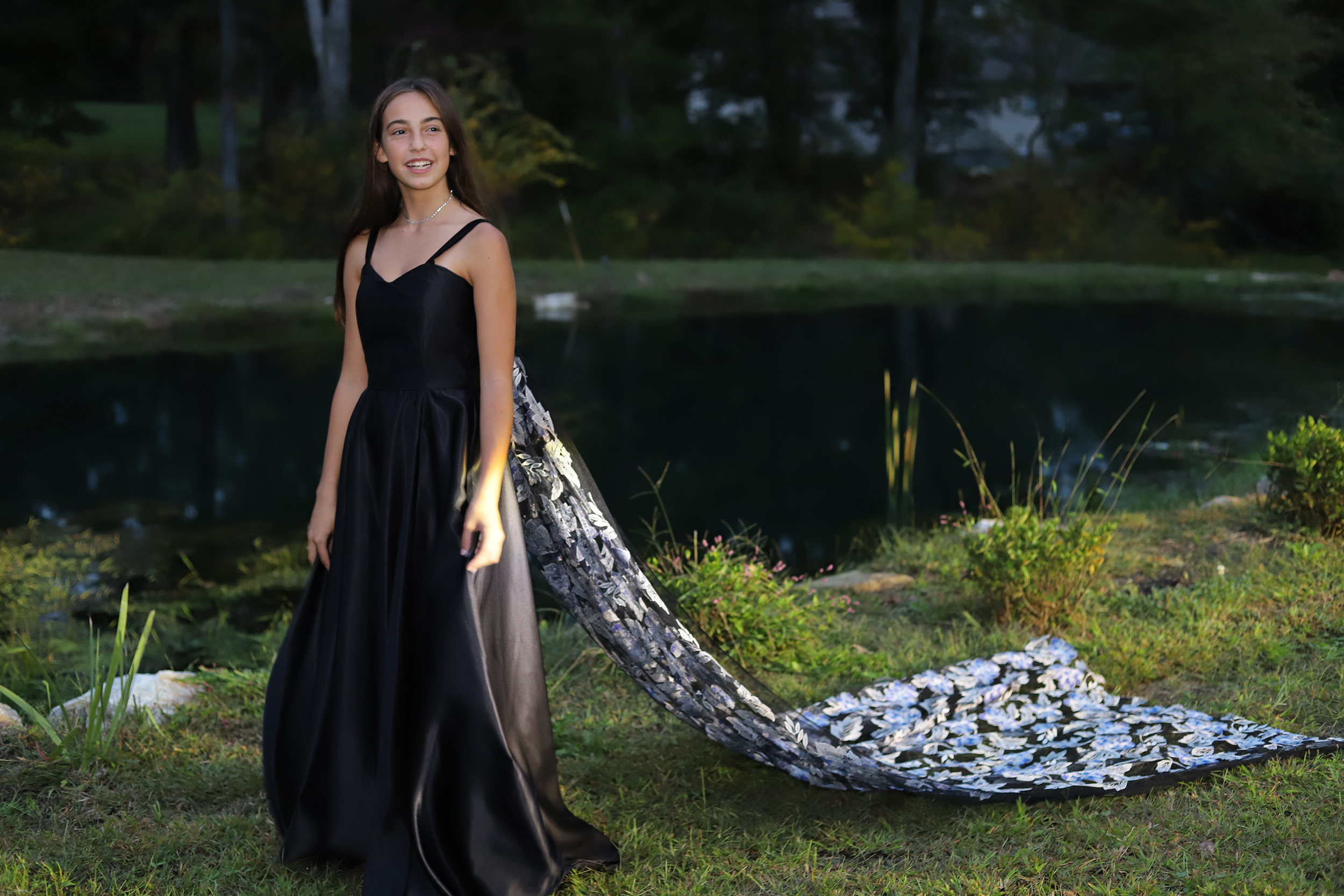 girl standing in grass in a black gown with a brace train